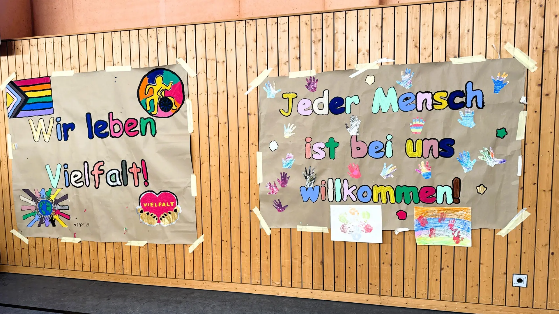 Plakate an der Wand mit der Aufschrift "Wir leben Vielfalt" und "Jeder Mensch ist bei uns willkommen"