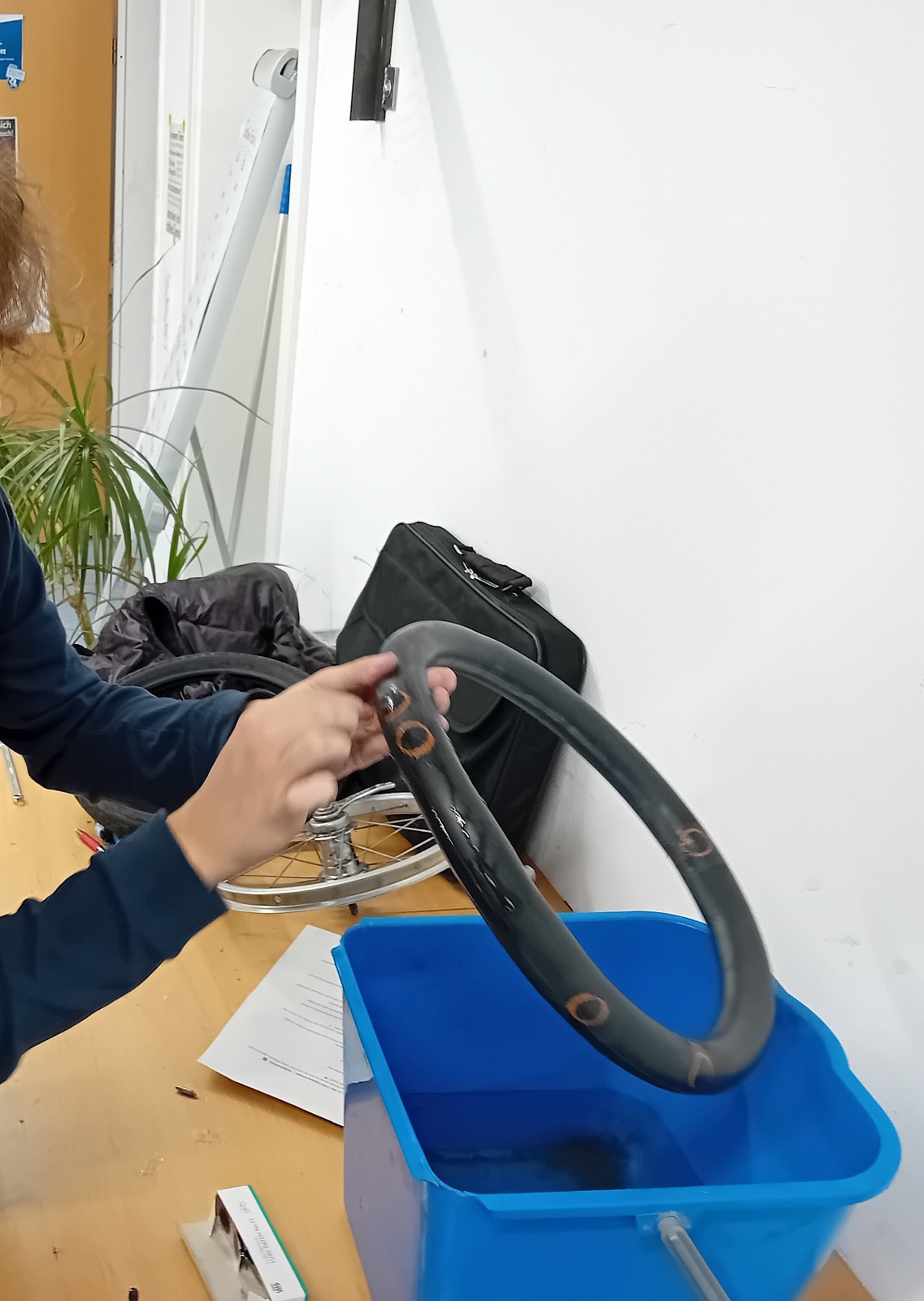 Ein Fahrradschlauch mit Flicken wird über eine Schüssel aus Wasser gehalten