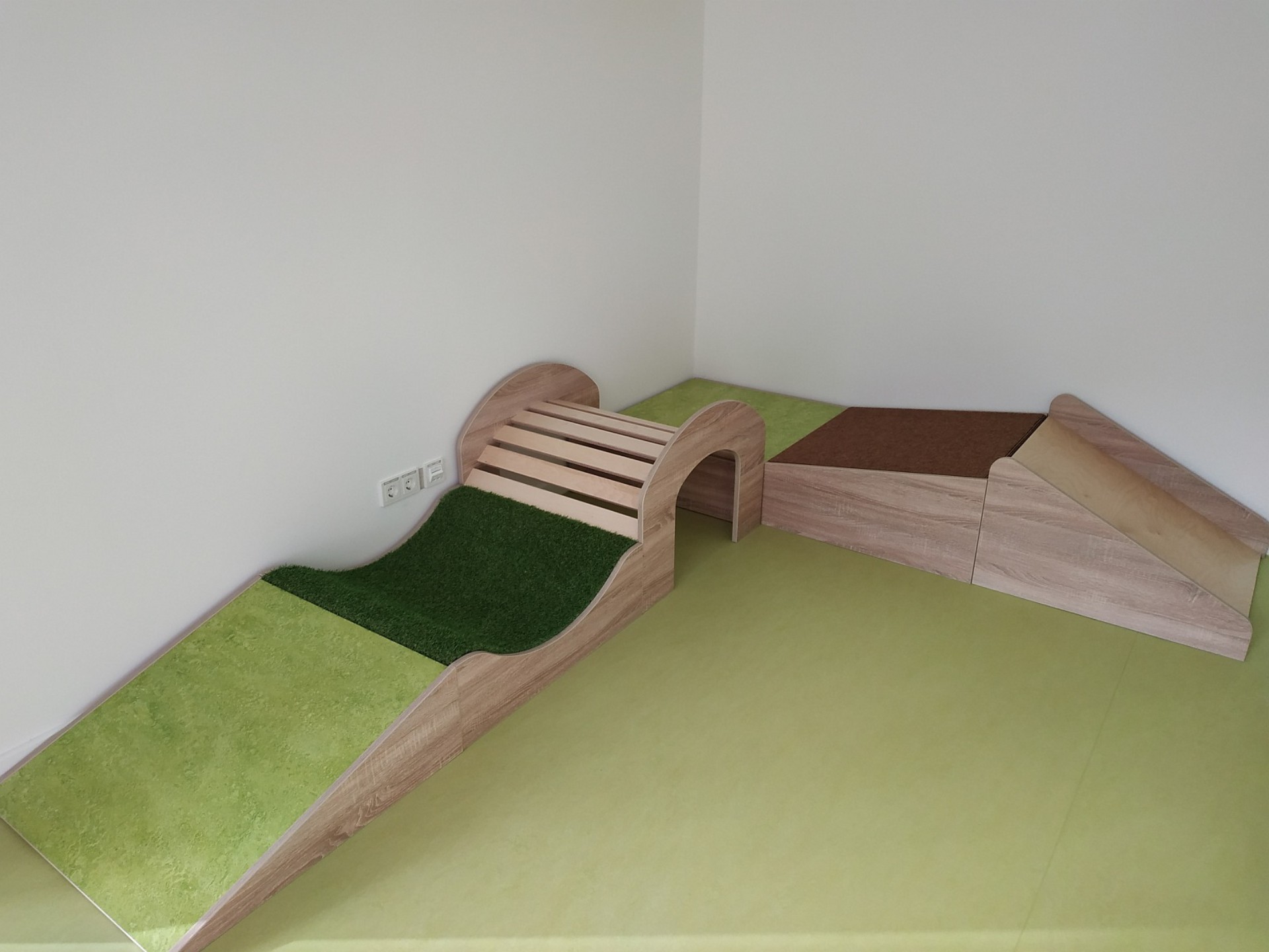 Detail in einem Kindergarten-Raum: ein kleiner Parcours mit Steigung und Brücke zum Bauen oder Laufen.