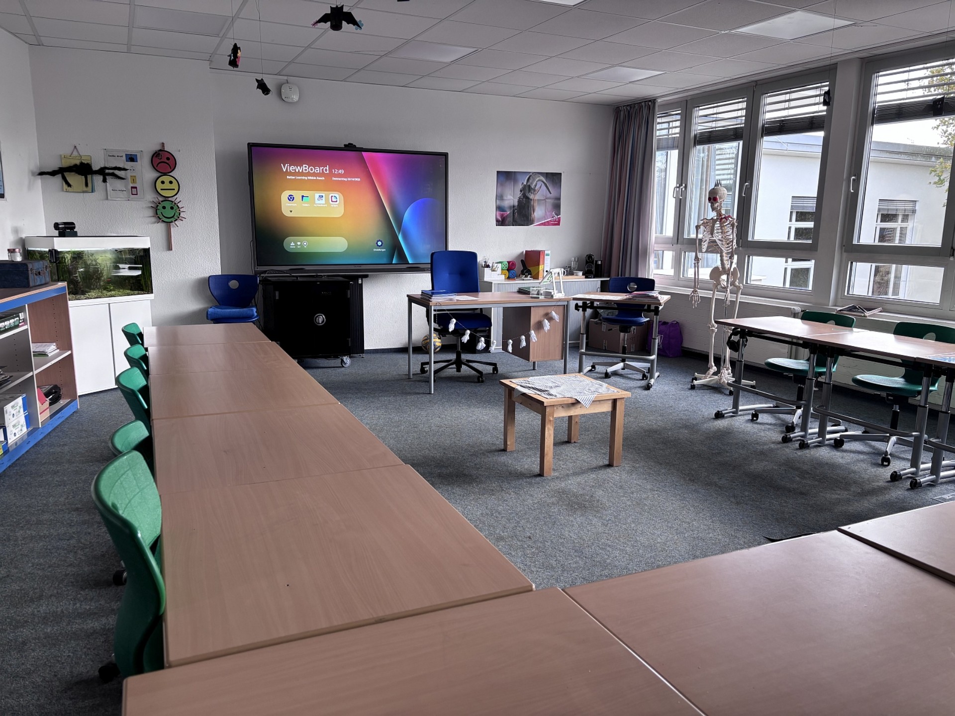 Ein Klassenraum mit Smartboard. Neben dem Pult steht ein Skelett.