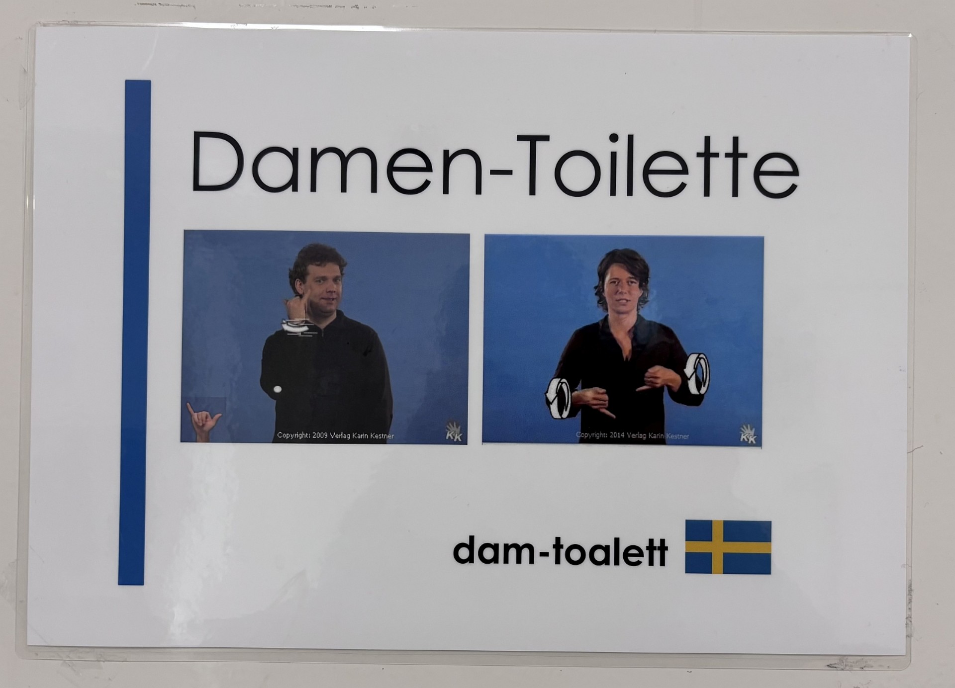 Schild "Damen-Toilette": In deutscher Schrift, als Gebärdenfotos und in schwedischer Schrift inklusive Landesflagge.