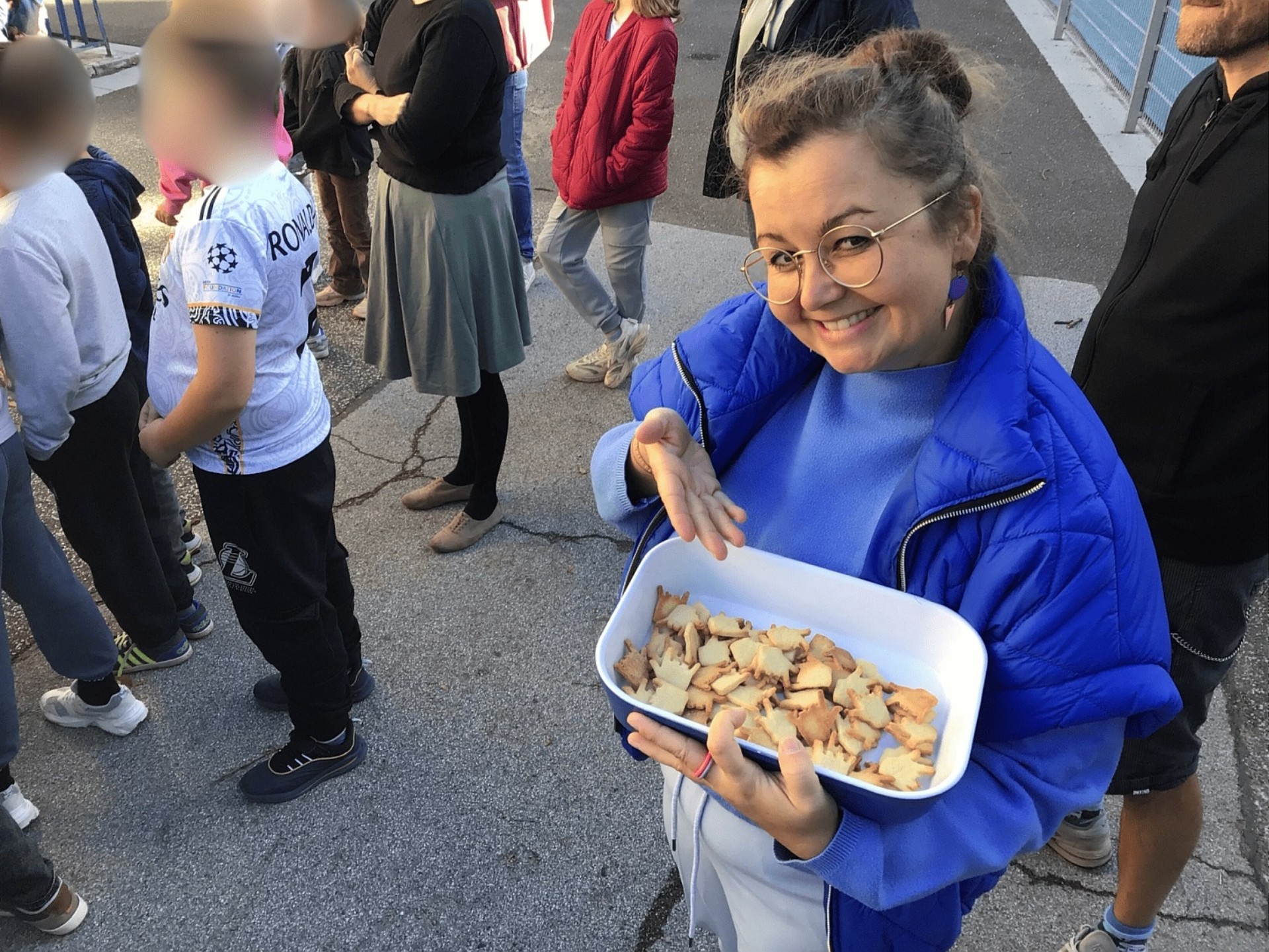 Eine Frau zeigt einladend auf eine Schüssel mit Keksen in Form der ILY_Hand.
