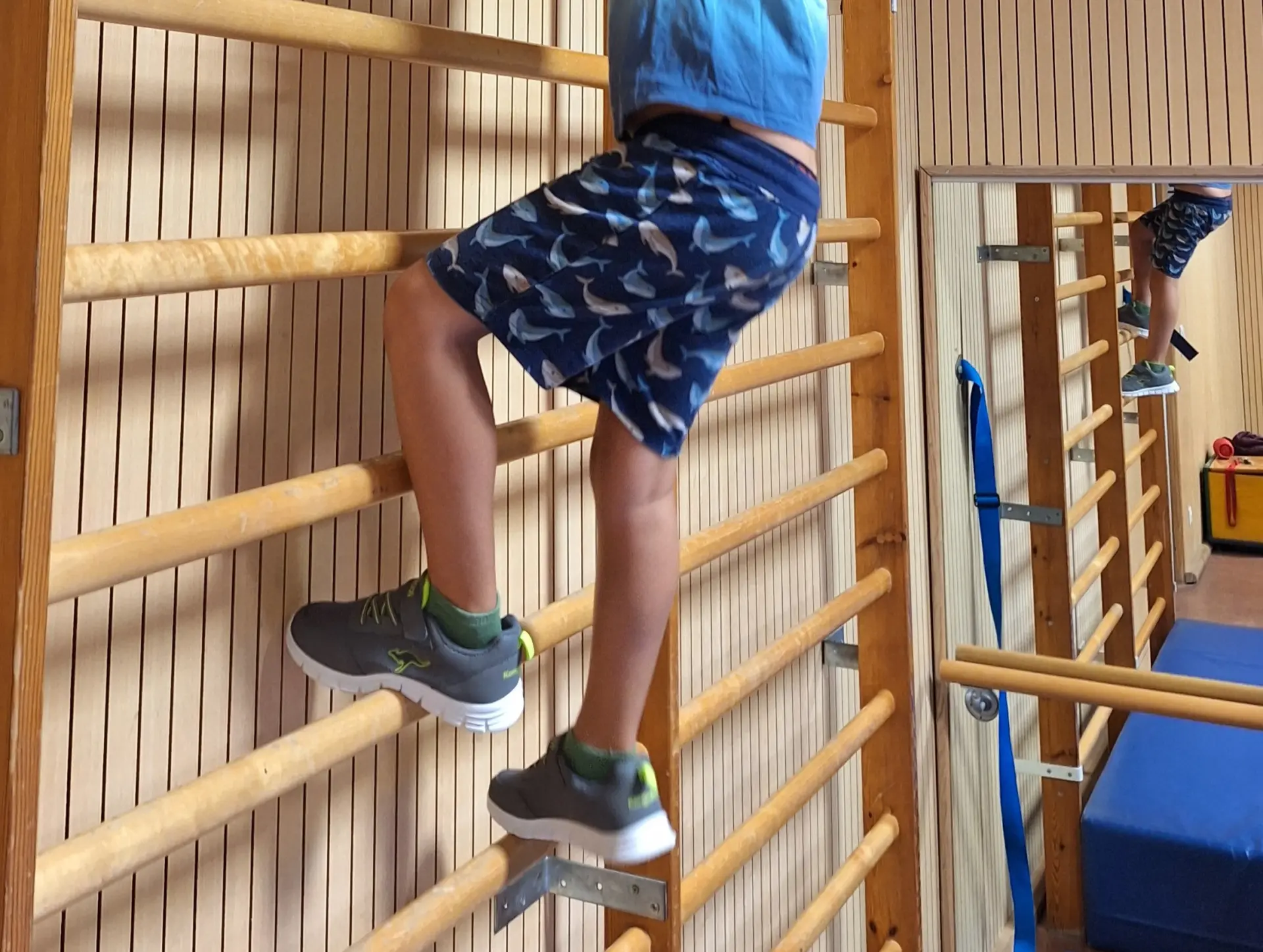 Kind klettert Sprossenwand in Turnhalle hoch