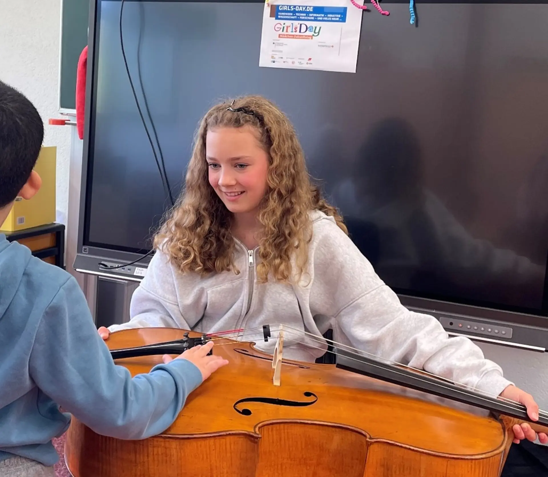 Mädchen mit Cello zeigt ihr Instrument einem Kind.