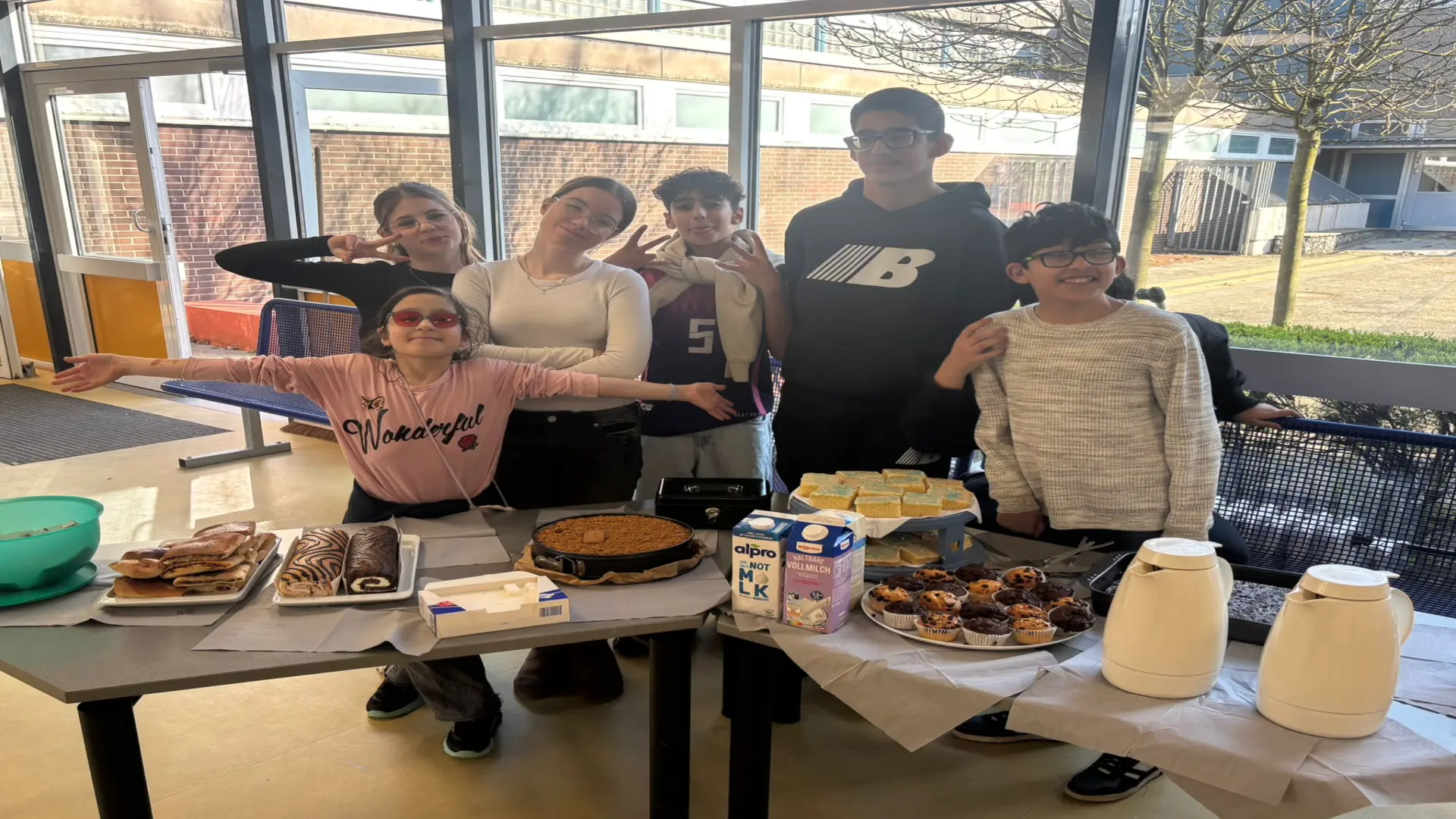 Schüler:innen stehen hinter einem Tisch auf welchem Kuchen, Kaffee etc. steht