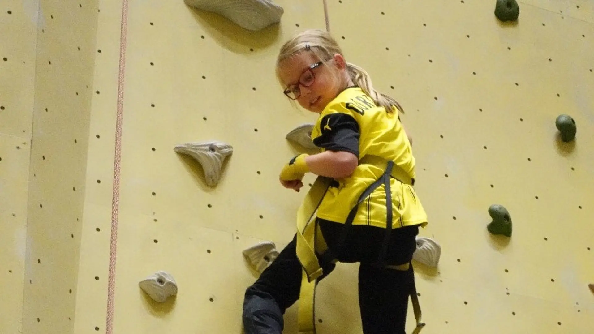 Schülerin klettert abgesichert eine Kletterwand hoch. 