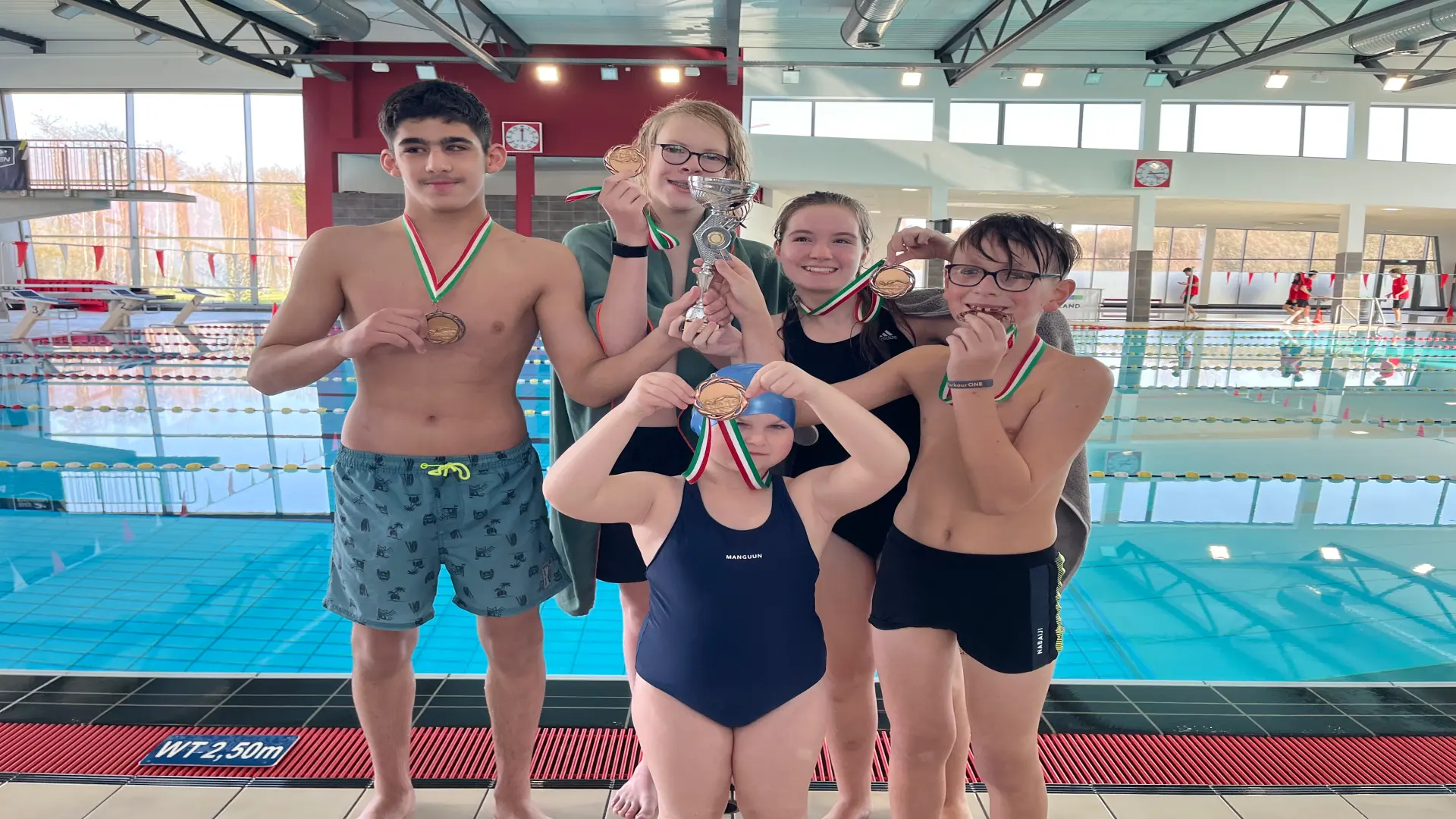 Schülerinnen und Schüler stehen vor einem Schwimmbecken und tragen stolz ihre Medaillen