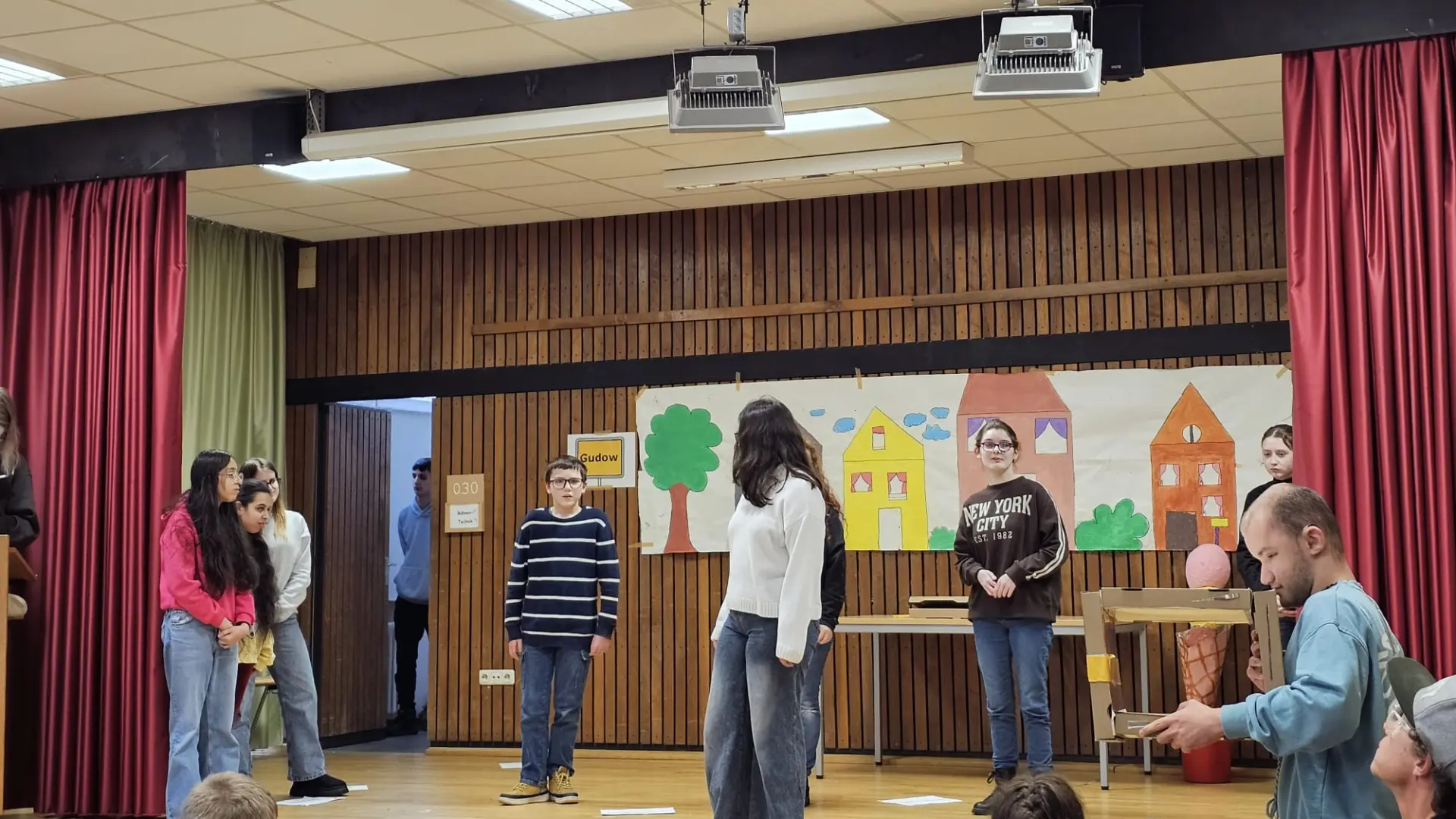 Mehrere Schülerinnen und Schüler stehen auf der Bühne und führen ein Theaterstück auf. 