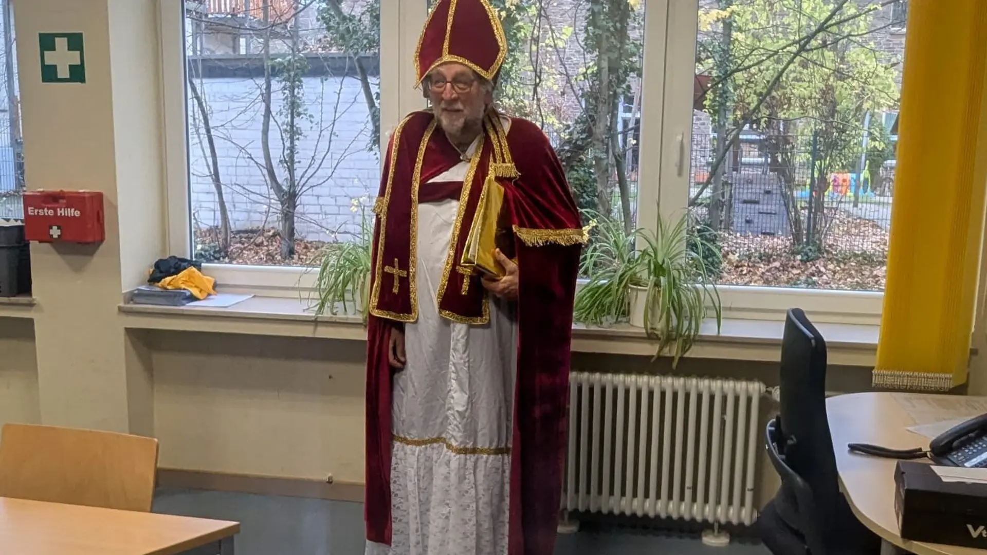 Ein älterer Herr steht, in ein Nikolauskostüm gekleidet, vor einer Fensterbank.