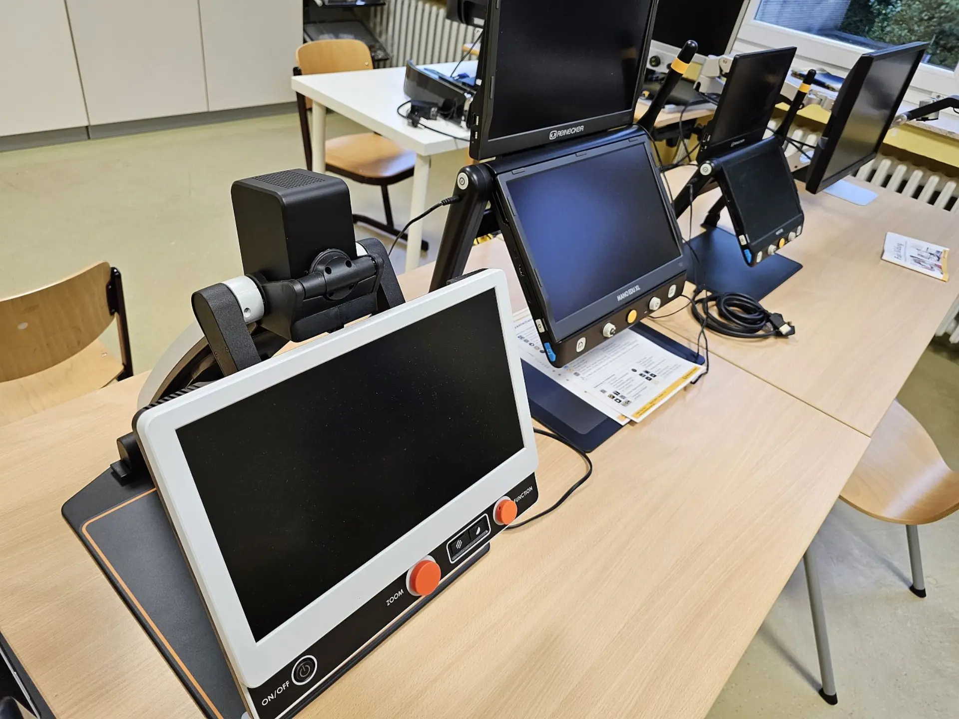 In einem Klassenraum sind auf mehreren Tischen unterschiedliche Bildschirmgeräte zu sehen.