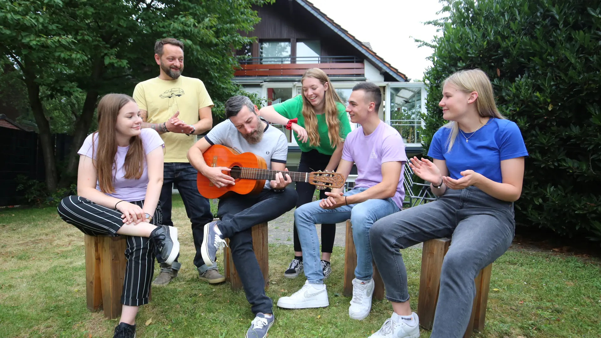 sechs Teenager sitzen mit Gitarre zusammen im Garten