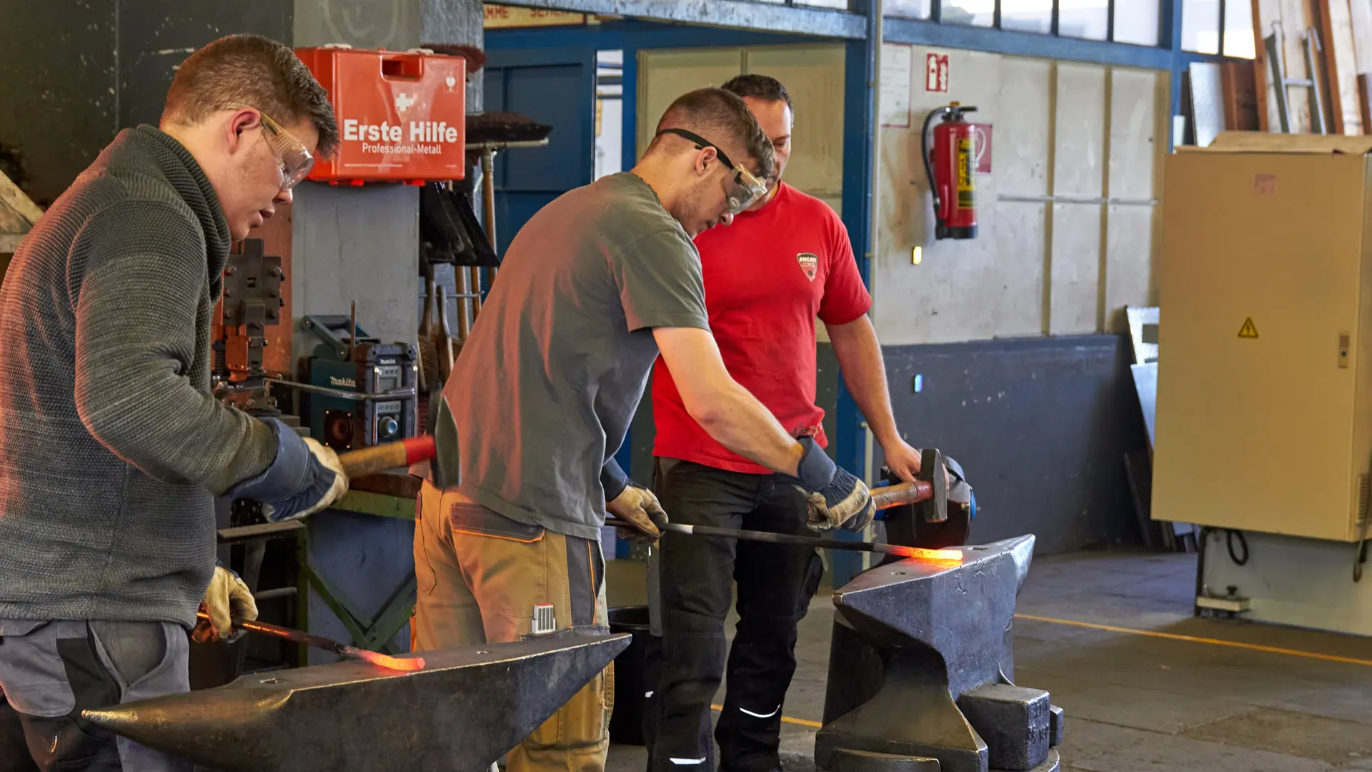 drei Männer arbeiten mit glühenden Metallstangen