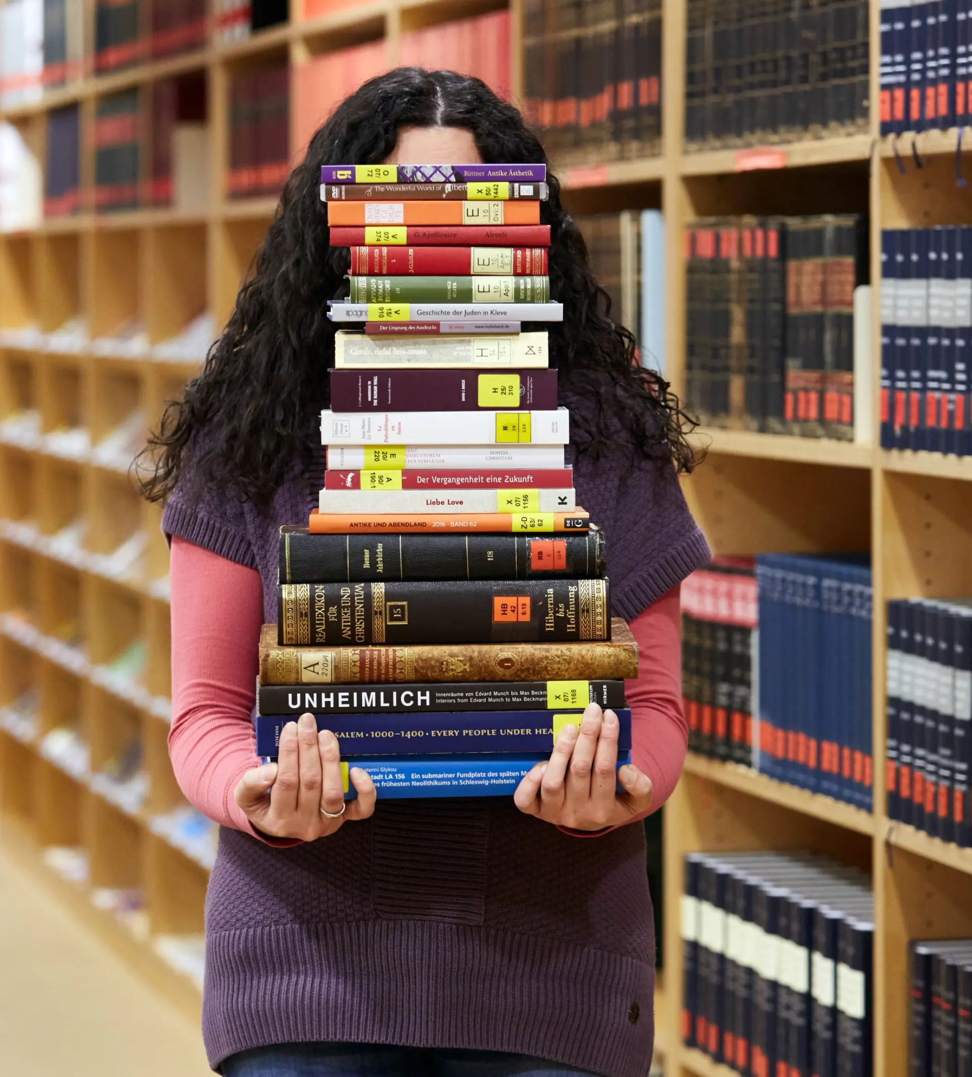 Eine Person trägt einen Stapel unterschiedlicher Bücher.