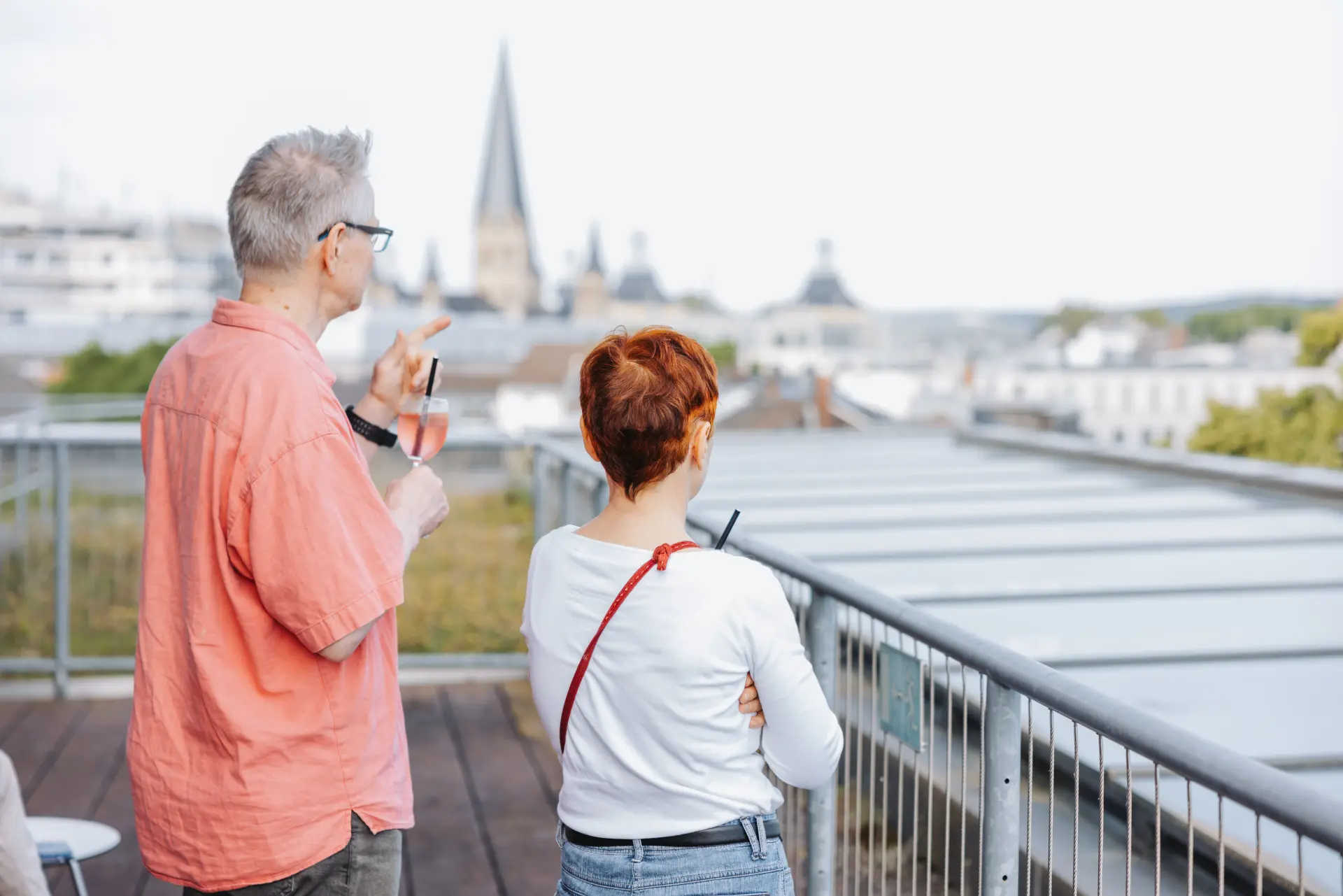 Ein Pärchen mit Cocktails auf der Dachterrasse mit Stadtblick auf den Bonner Münster.