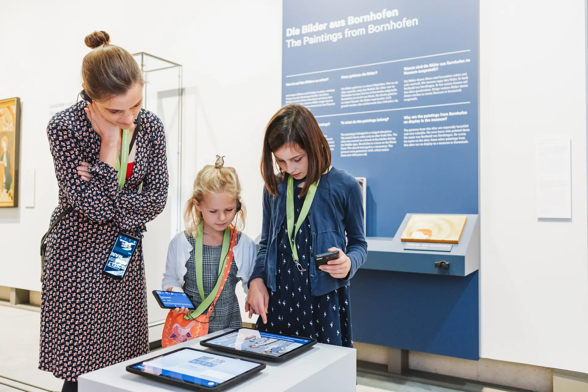 Zwei Mädchen und eine Frau schauen zusammen auf ein Tablet in der Dauerausstellung des Landesmuseums.