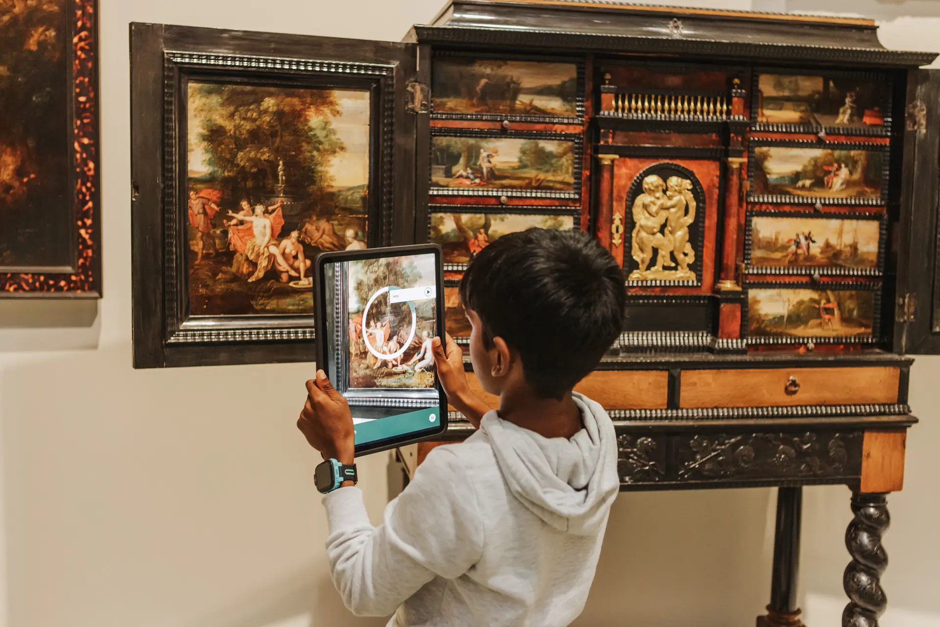 Ein Junge scannt mit einem Tablet einen Tisch in der Ausstellung, um mehr Informationen über das Objekt zu erhalten.