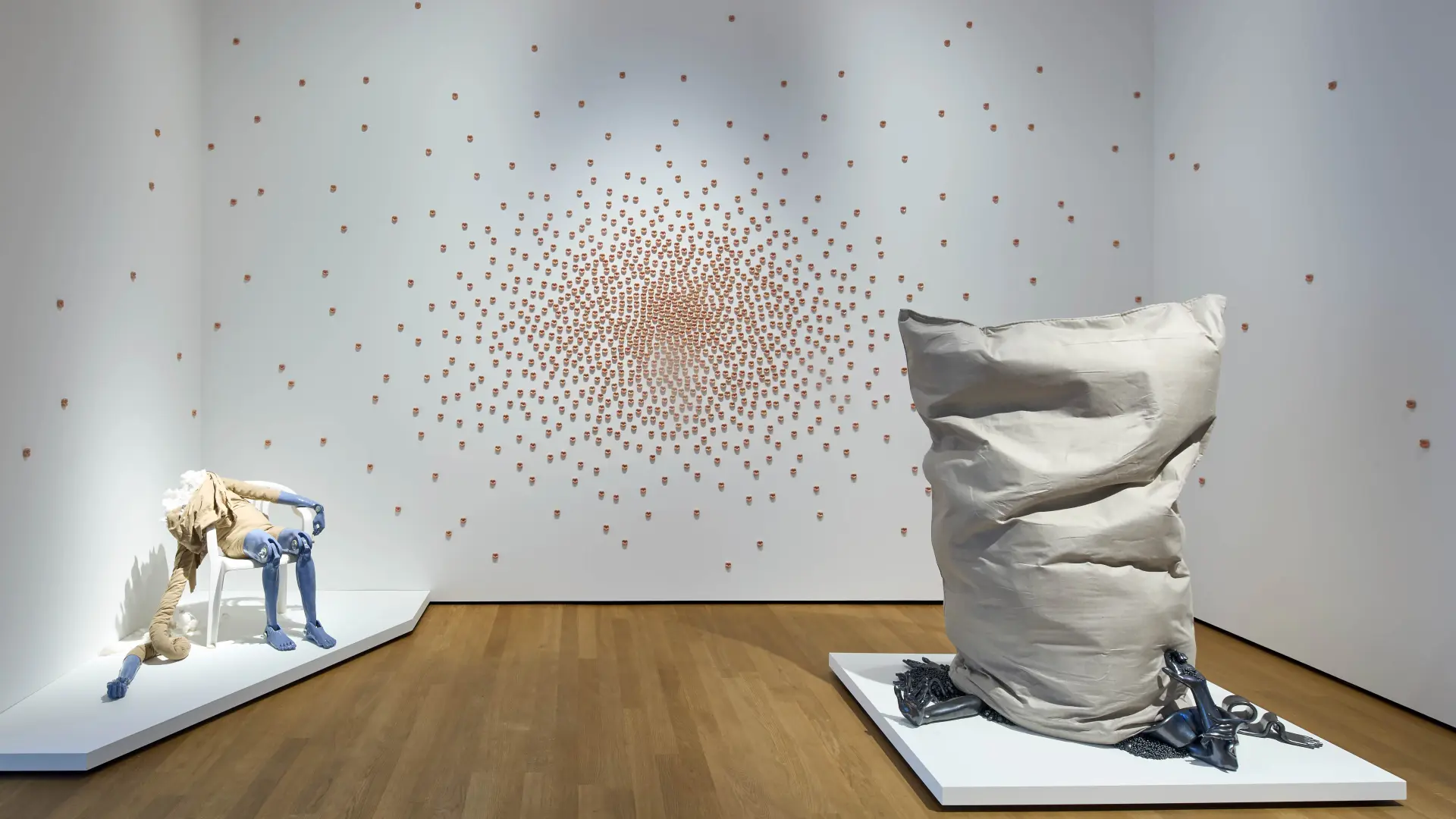Drei Kunstwerke von Isabell Kamp im Landesmuseum: Eine kopflose Figur auf einem Stuhl sitzend, ein großer Sack, der auf Ketten und Armen steht und an der Wand 1000 Kussmünder aus Ton gefertigt.