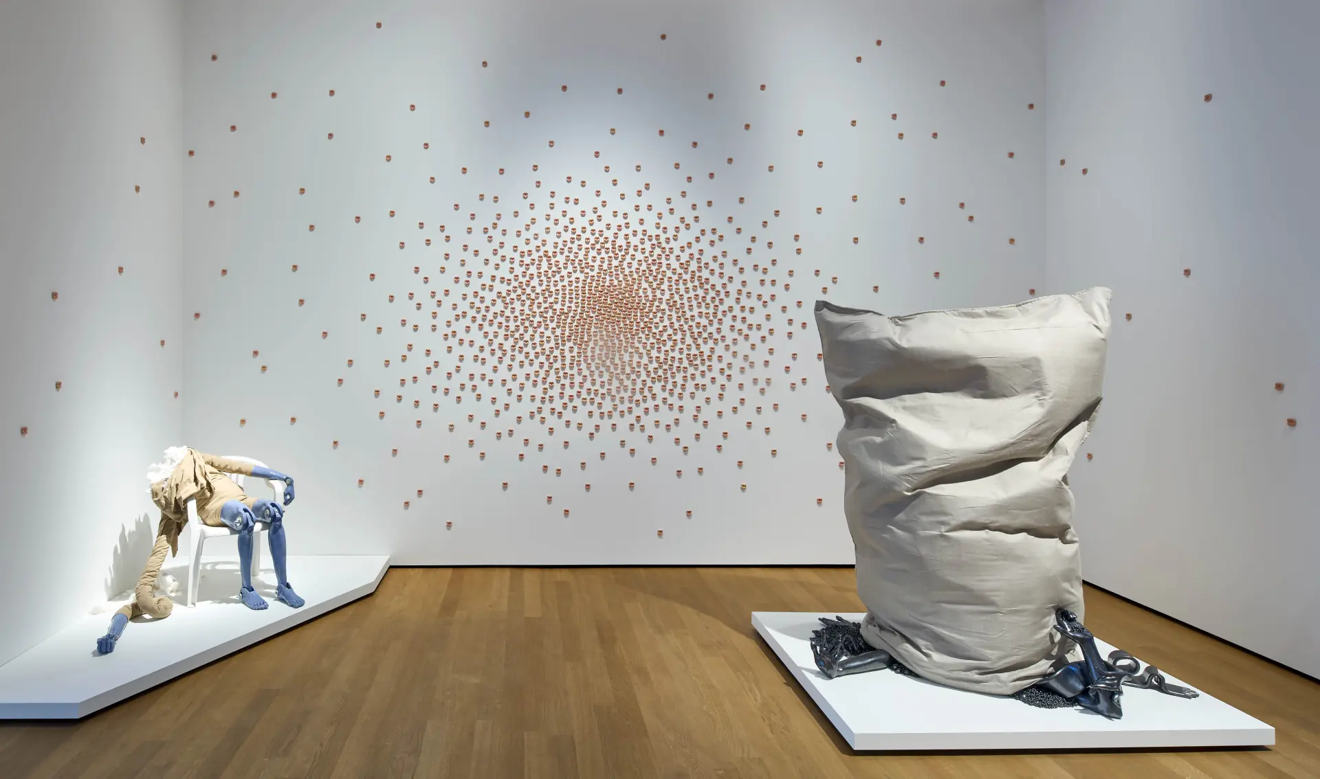 Drei Kunstwerke von Isabell Kamp im Landesmuseum: Eine kopflose Figur auf einem Stuhl sitzend, ein großer Sack, der auf Ketten und Armen steht und an der Wand 1000 Kussmünder aus Ton gefertigt.