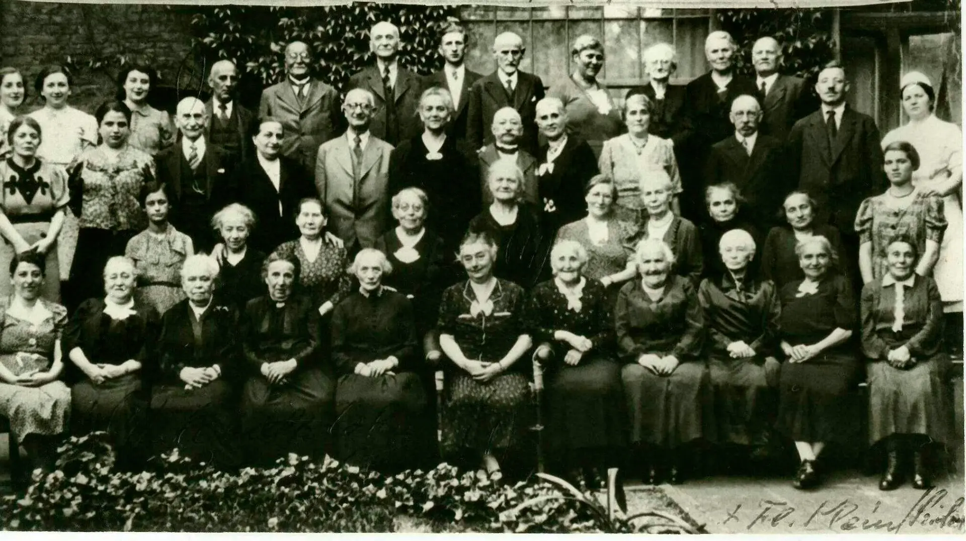 Schwarz-weiß Fotografie der Bewohnerinnen des Altenheim in Rheyd. Mehre Menschen stehen in vier Reihen und posieren für das Foto. In der Mitte ist Sibilla Ullmann zu sehen.