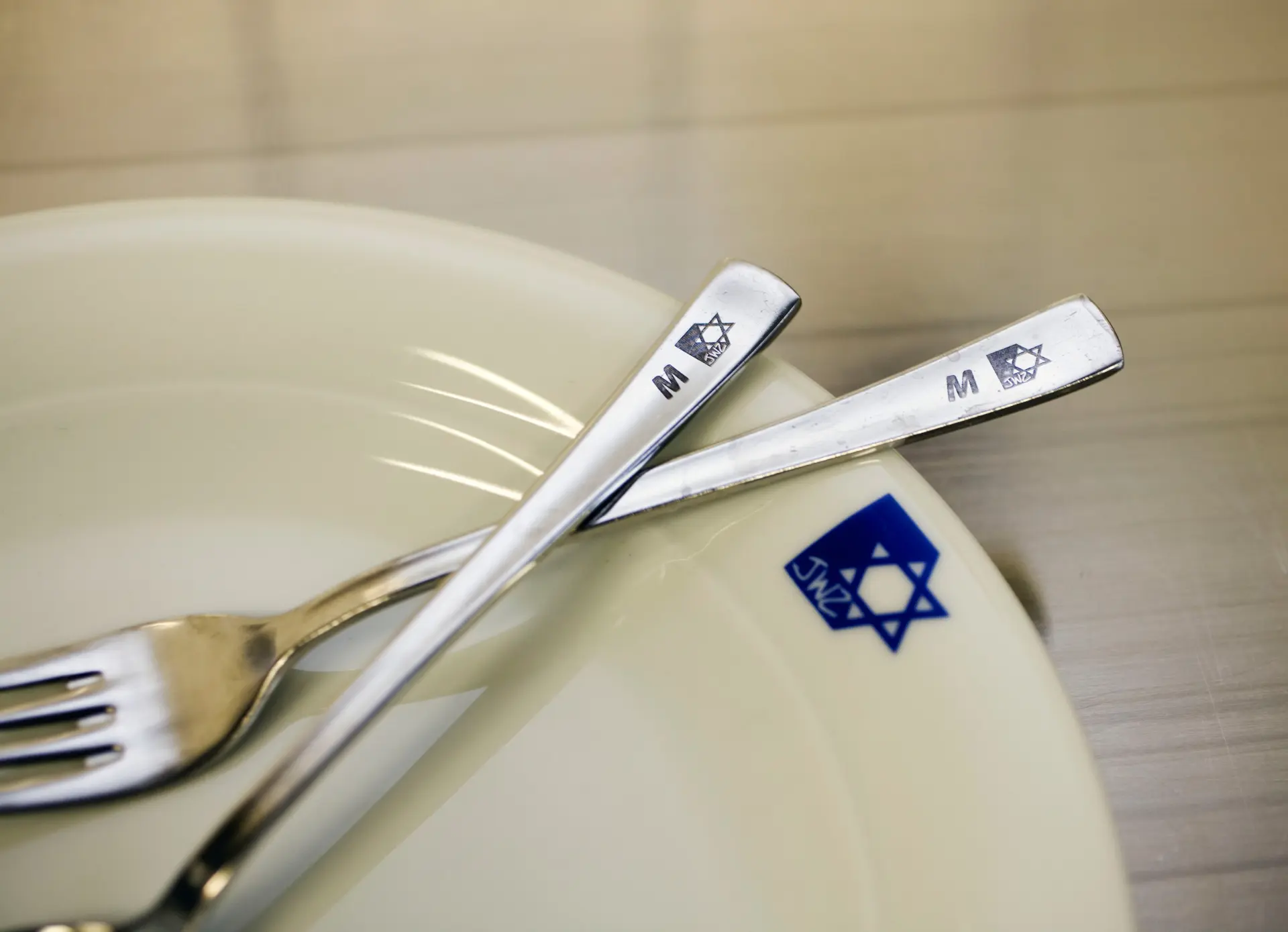 Ein weißer Teller mit blauer Markierung. Auf dem Teller liegen eine Gabel und ein Löffel.
