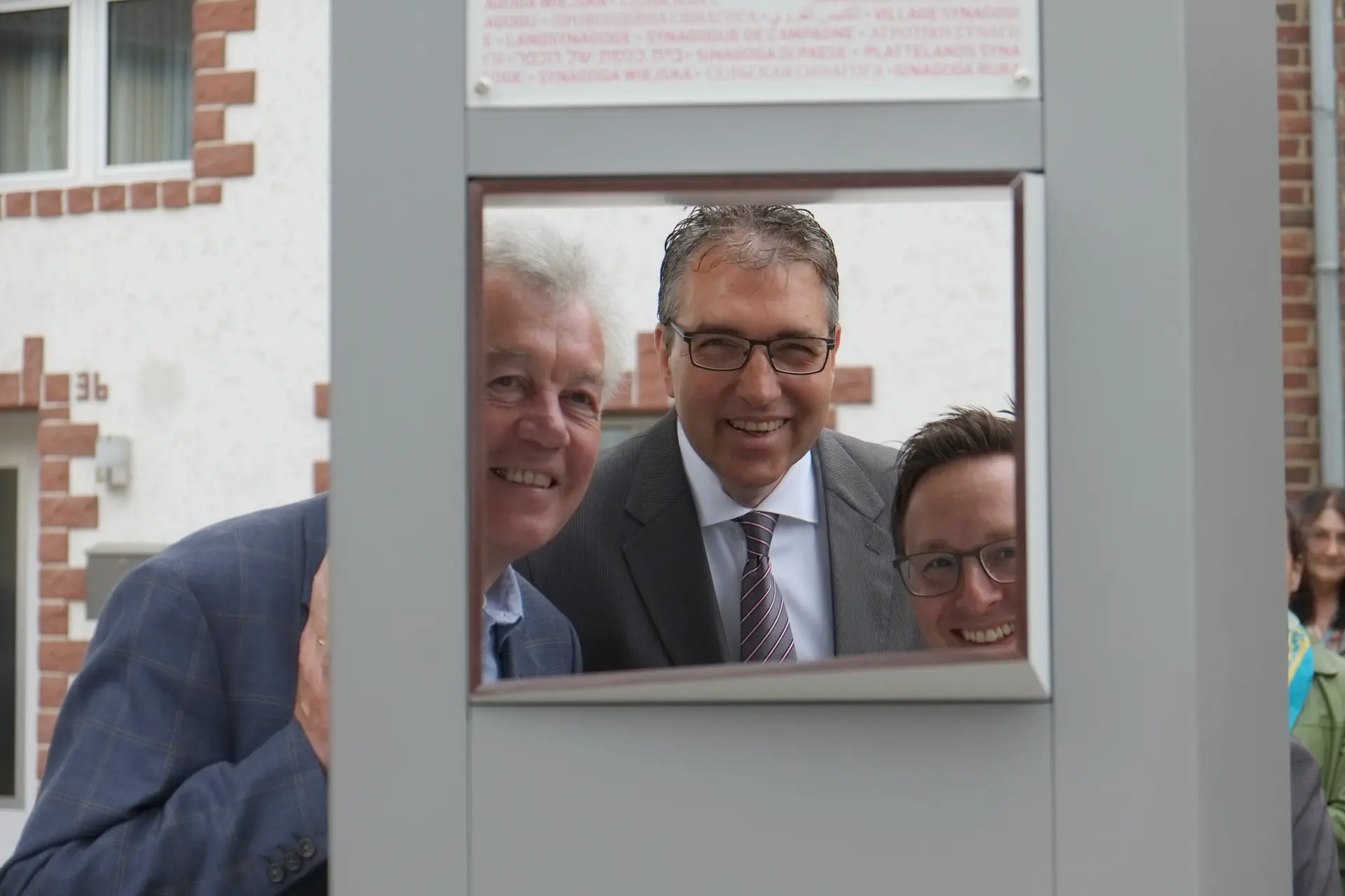 Drei Männer schauen durch das Guckfenster der Informationsstele "Landsynagoge"