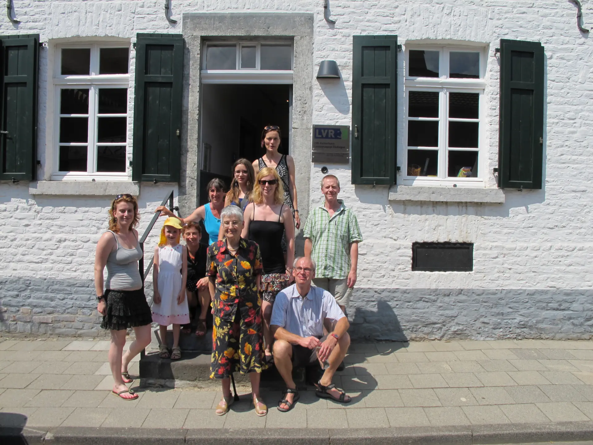 Zehn Personen posieren für ein Foto auf Treppenstufen vor dem Eingang zu einem weiß getünchten Wohnhaus.