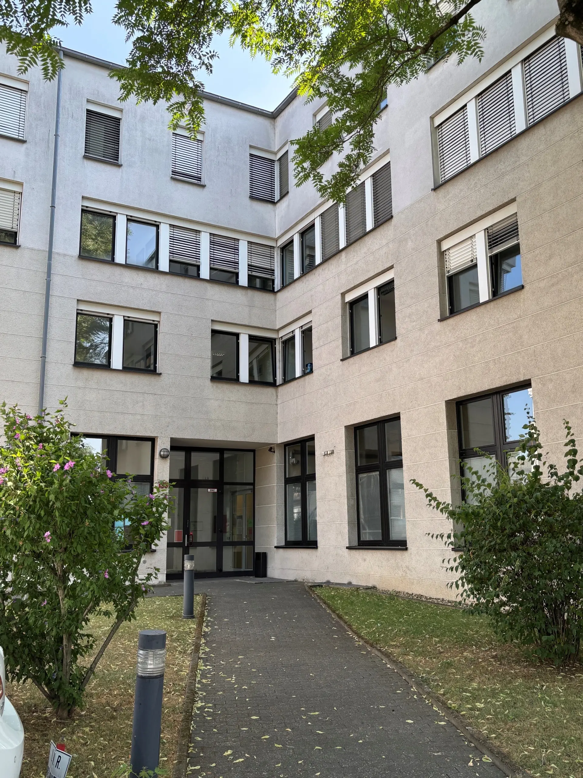 Die Front eines Bürogebäudes mit vier Geschossen. Das Gebäude ist grau und hat viele Fenster mit schwarzen Fensterrahmen.