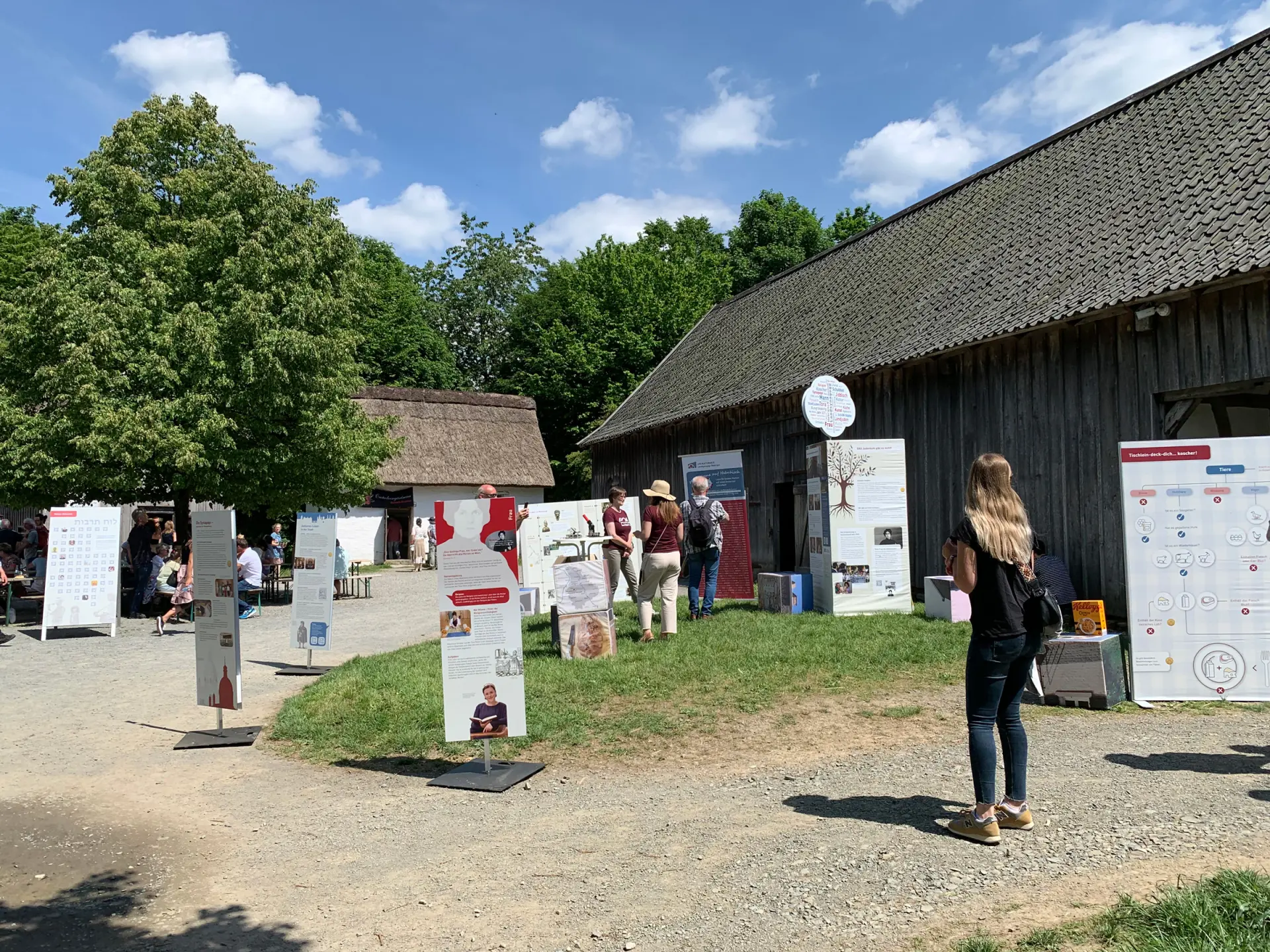 Vor einer alten Scheune stehen illustrierte Aufsteller einer Wanderausstellung