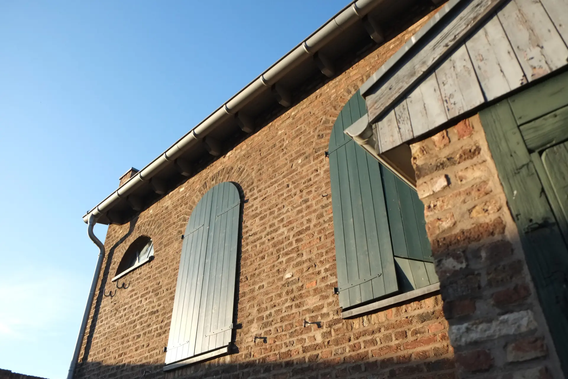 Eine Gebäudewand in Herbstsonne getaucht mit einem hochrechteckigen Fensterpaar. Geschlossene Fernsterläden verdecken die Fenster.