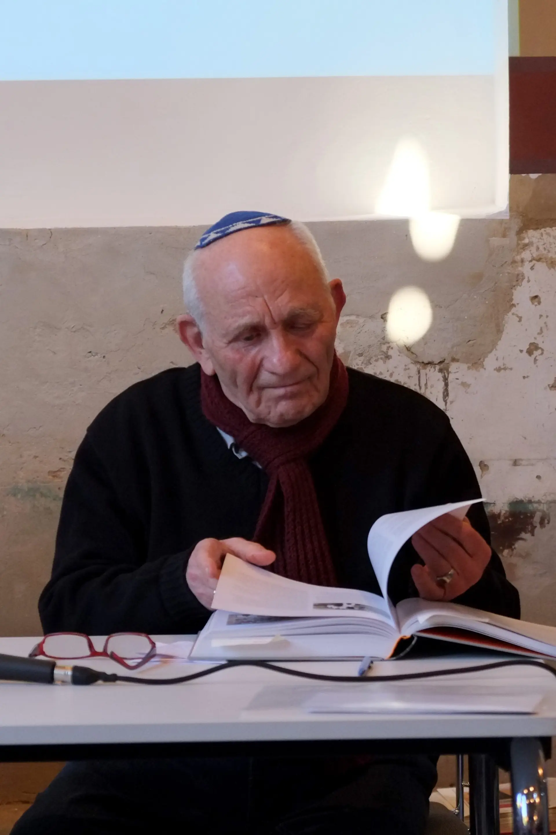 Ein älterer Mann mit Kippa liest aus einem Buch seine Lebensgeschichte