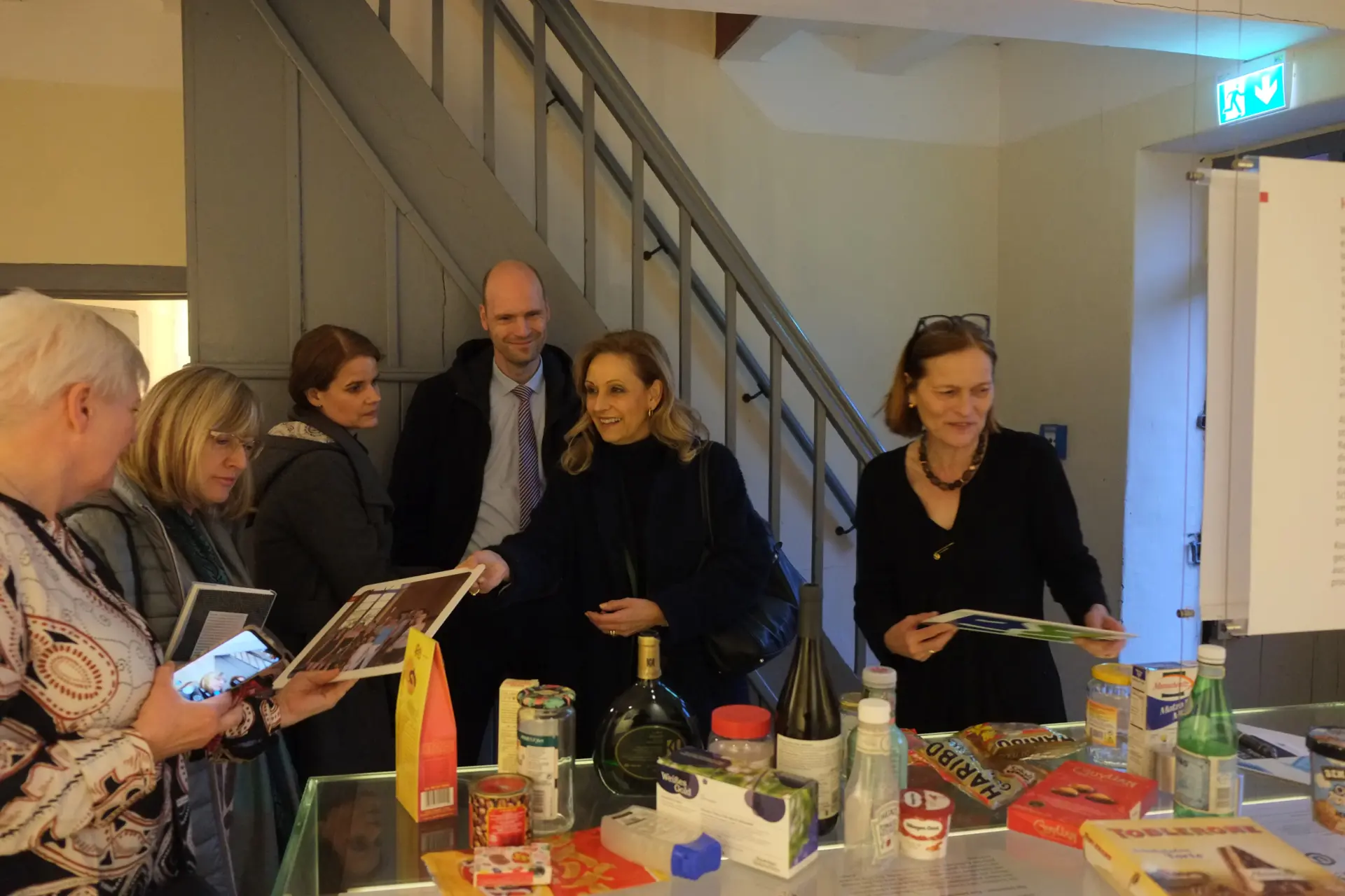 Mehrere Personen stehen im Ausstellungsraum koschere Küche um eine Vitrine, halten Lebensmittelpackungen in den Händen und betrachten diese.