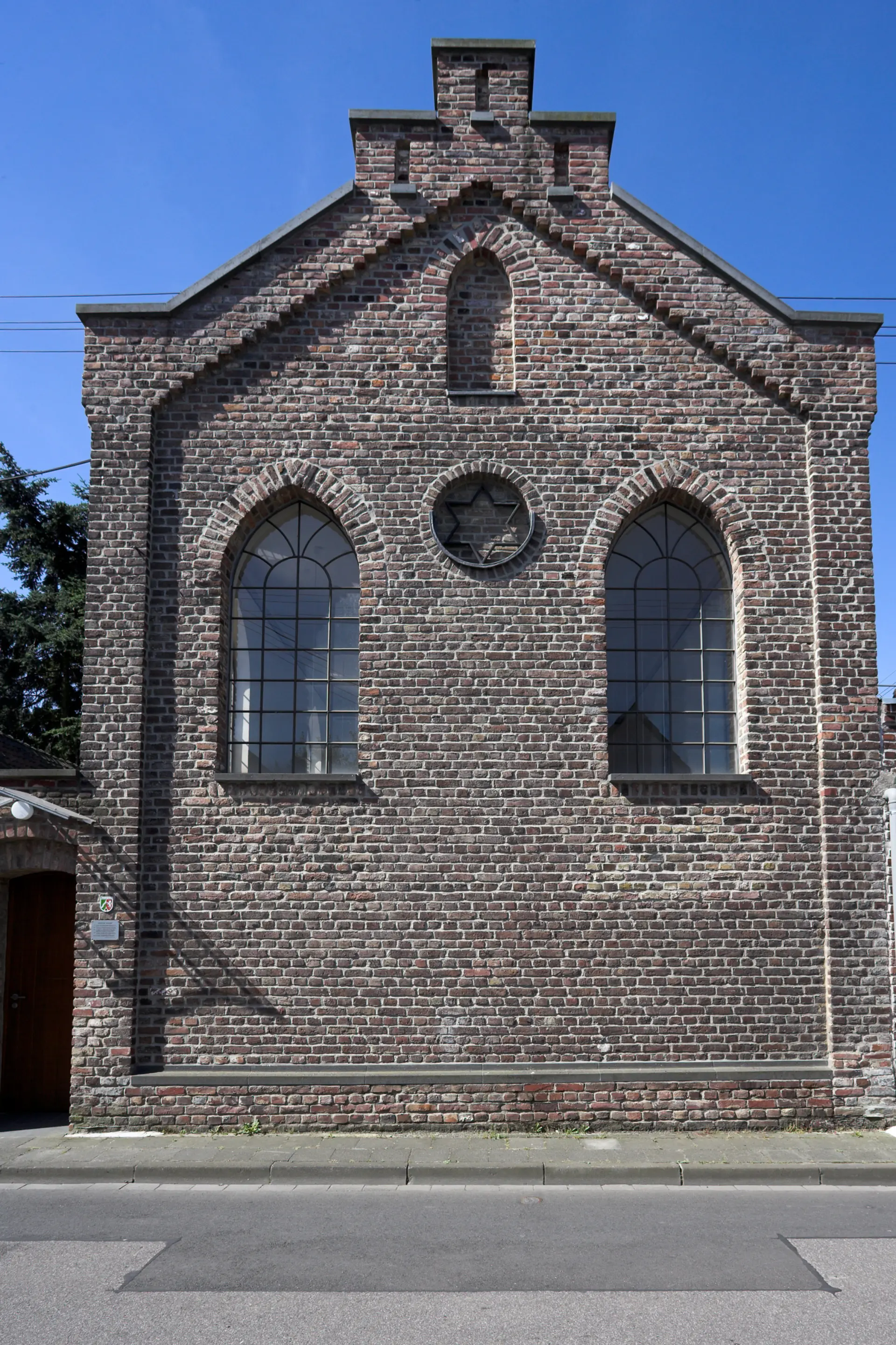 Frontseite eines Gebäudes mit Giebel und hohen Fenstern. In der Wand ist ein Davidstern in eine Vertiefung eingelassen.