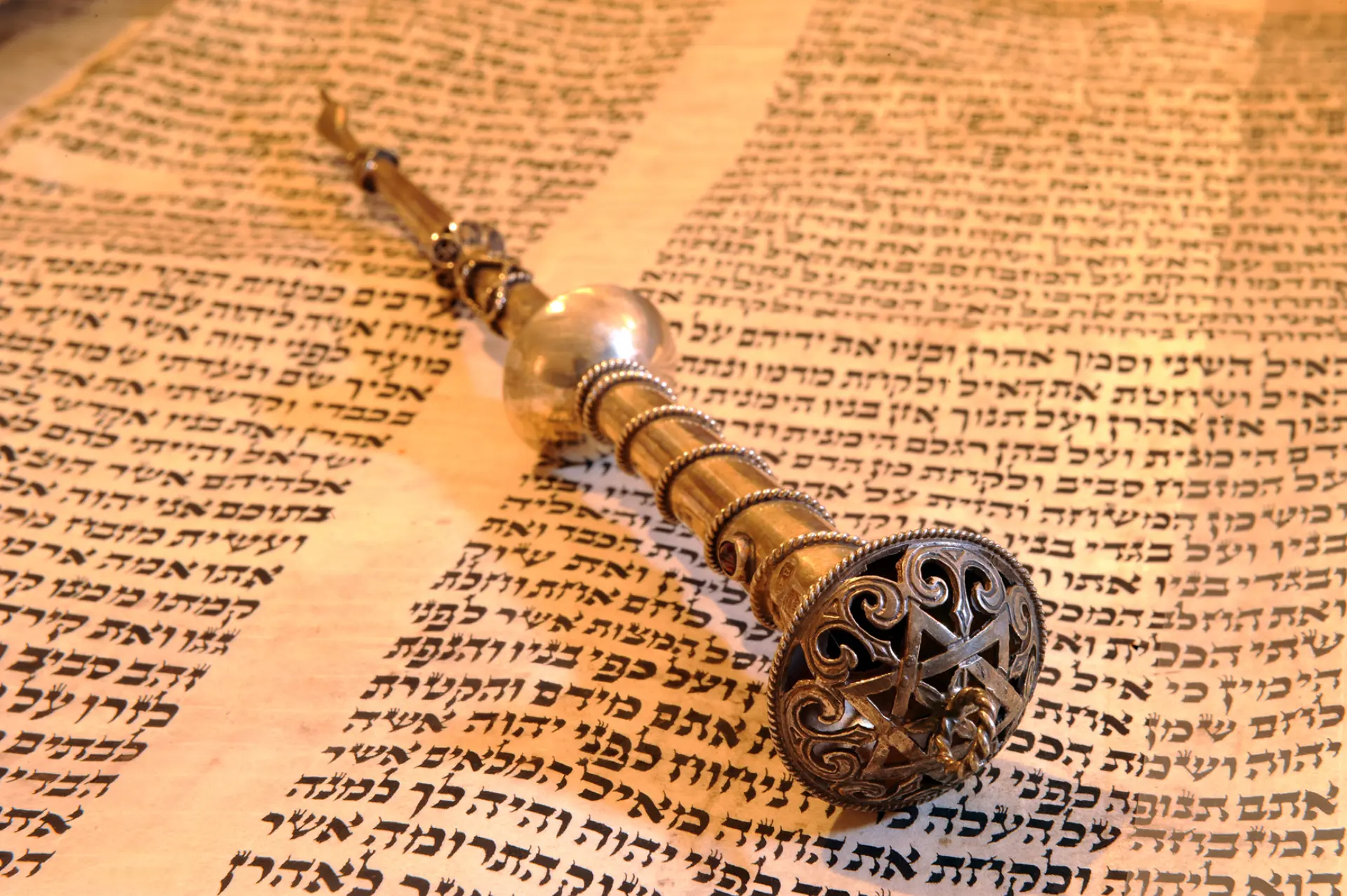 Ein Tora-Zeiger aus Silber, das ist ein Stab mit einer modellierten Hand an einem Ende, die einen Finger ausstreckt, liegt auf einem Torarollenfragment.