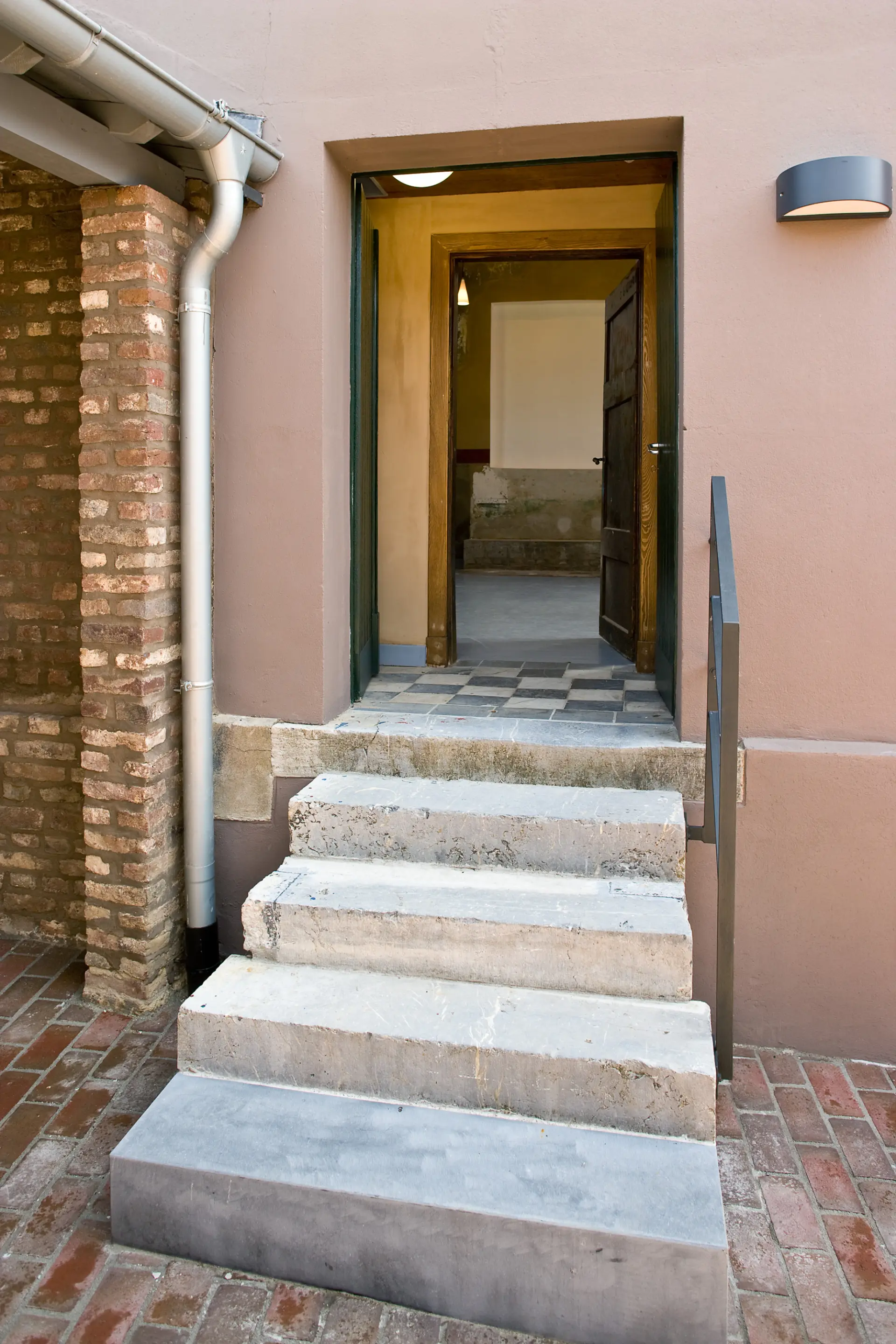 Treppenabsatz mit Eingang zur Synagoge. Durch zwei hintereinander geöffnete Türen kann man in den Innenraum der Synagoge blicken.