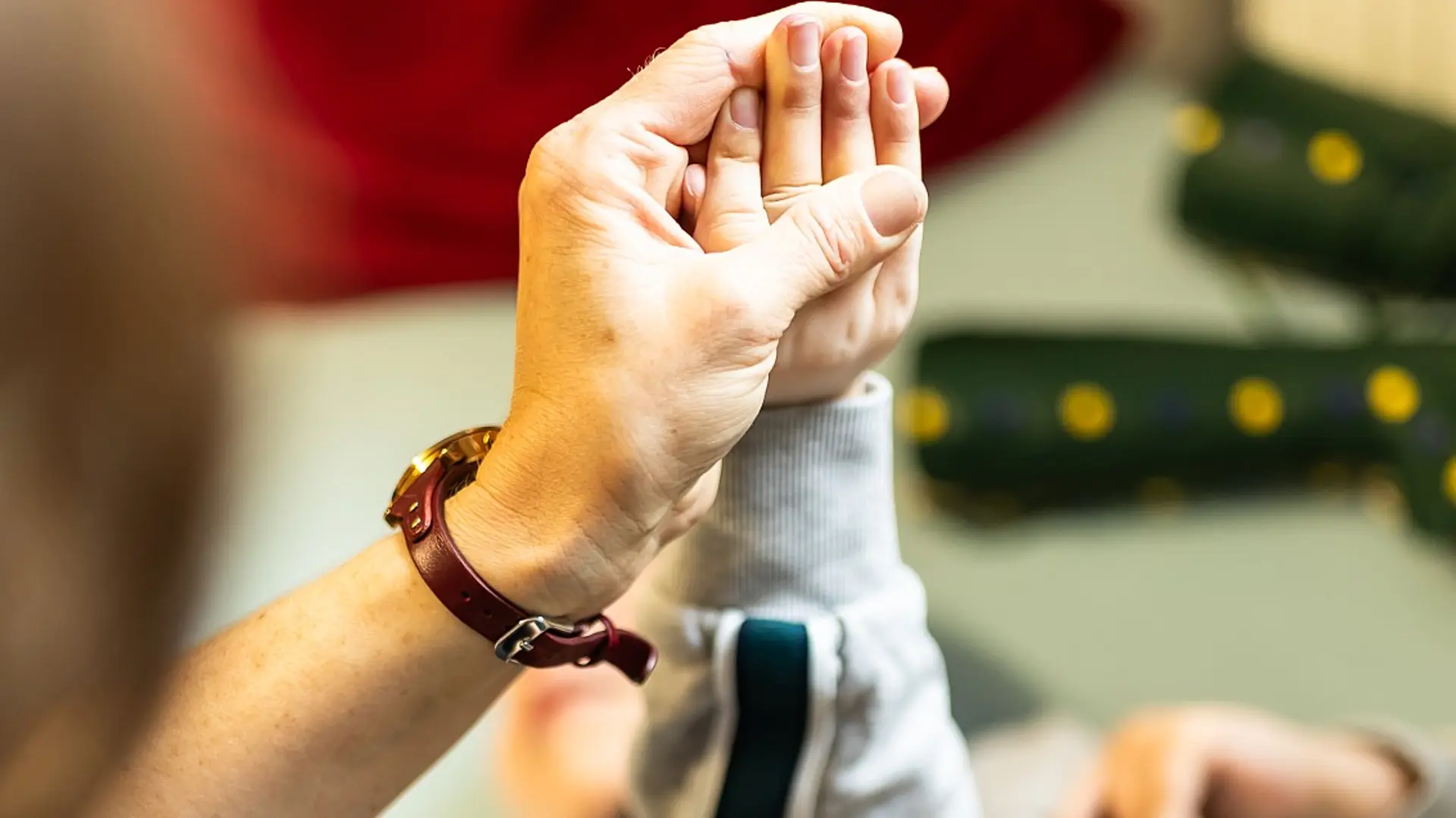 Physiotherapiestunde, in der eine therapeutische Fachkraft die Hand und den Arm eines liegenden Kindes vorsichtig hält und bewegt.