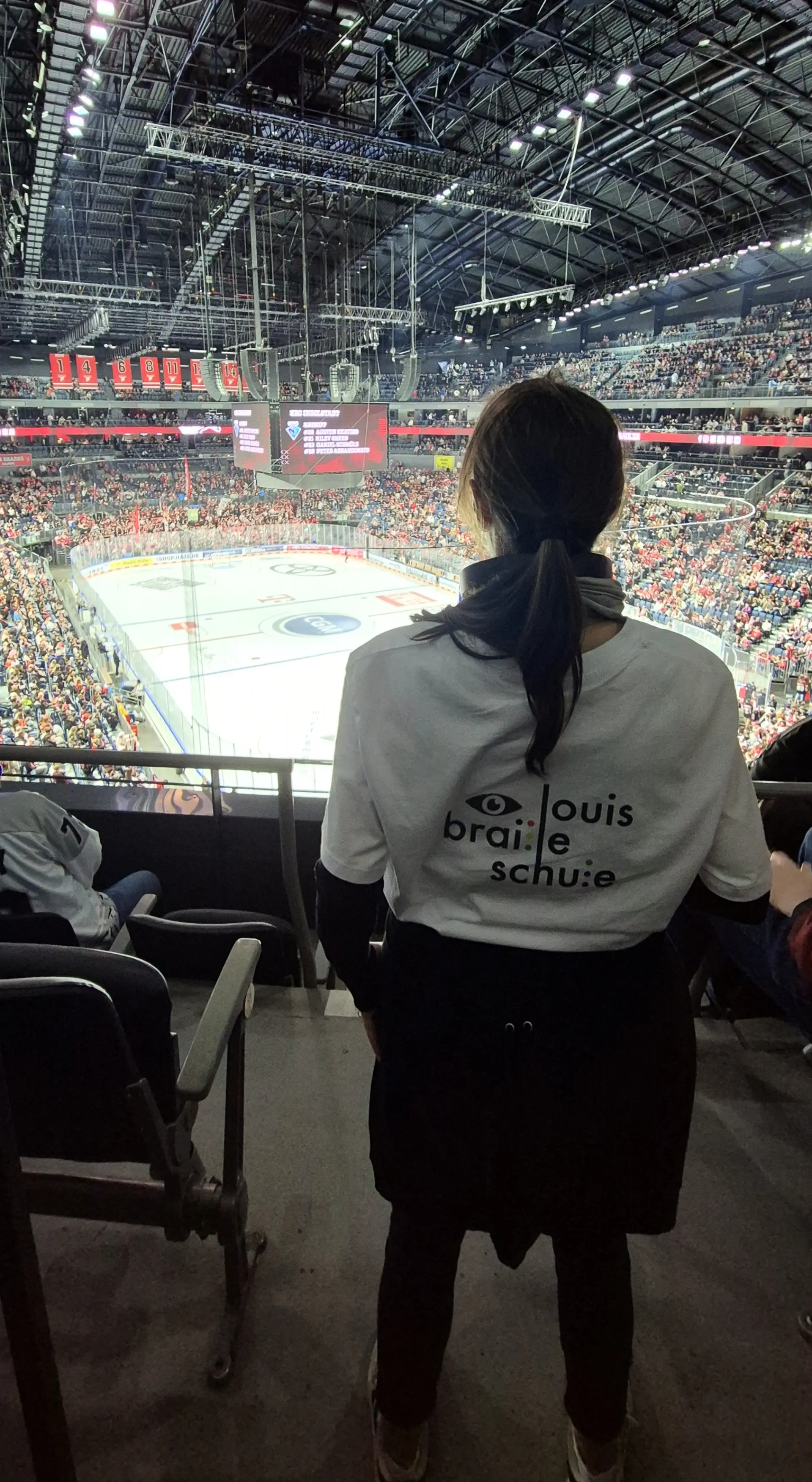 Person mit Blick auf Eisfläche im Hintergrund und Schullogo auf dem Rücken.