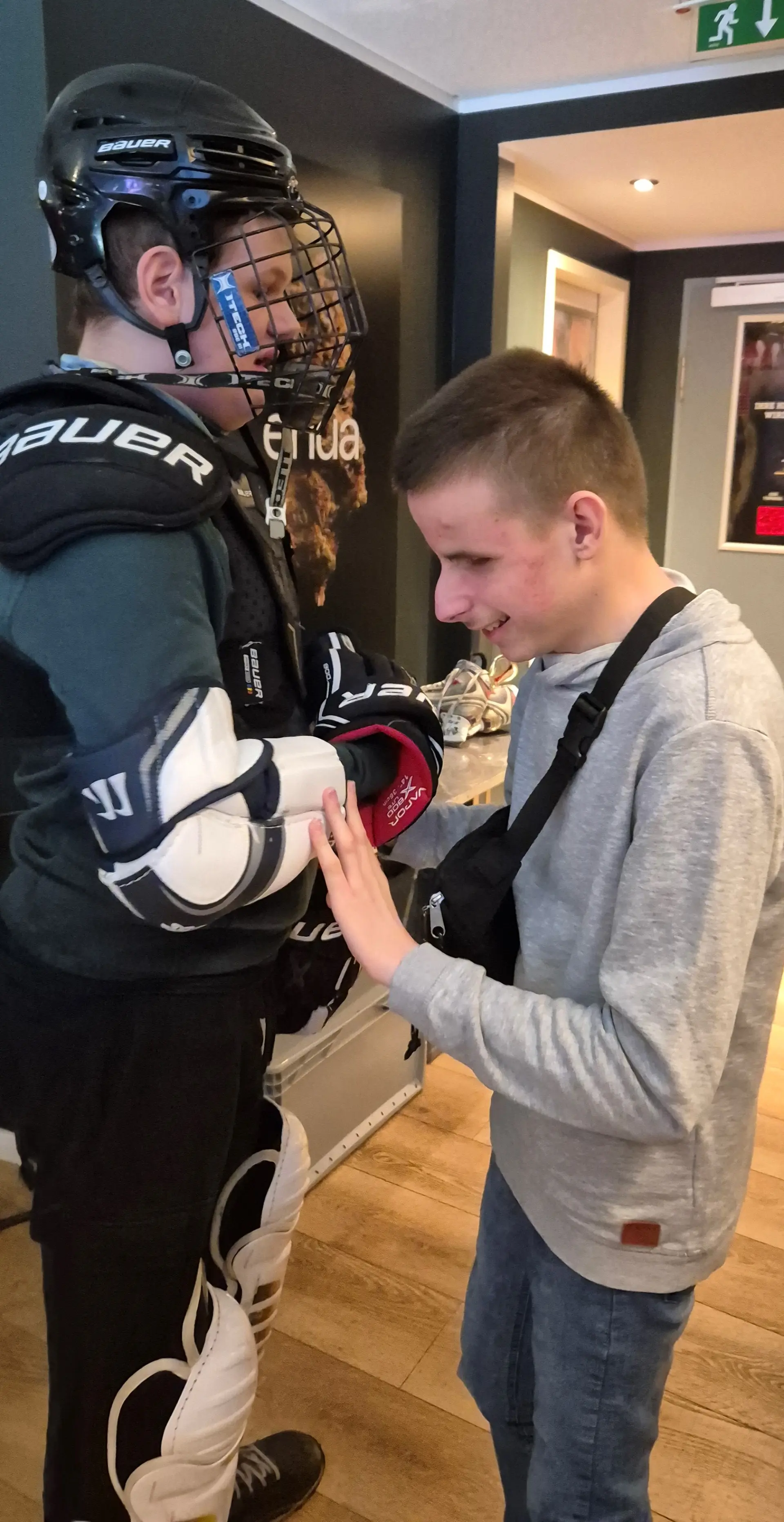 Schüler in voller Eishockeymontur, ein weiterer Schüler ertastet den Armschutz.
