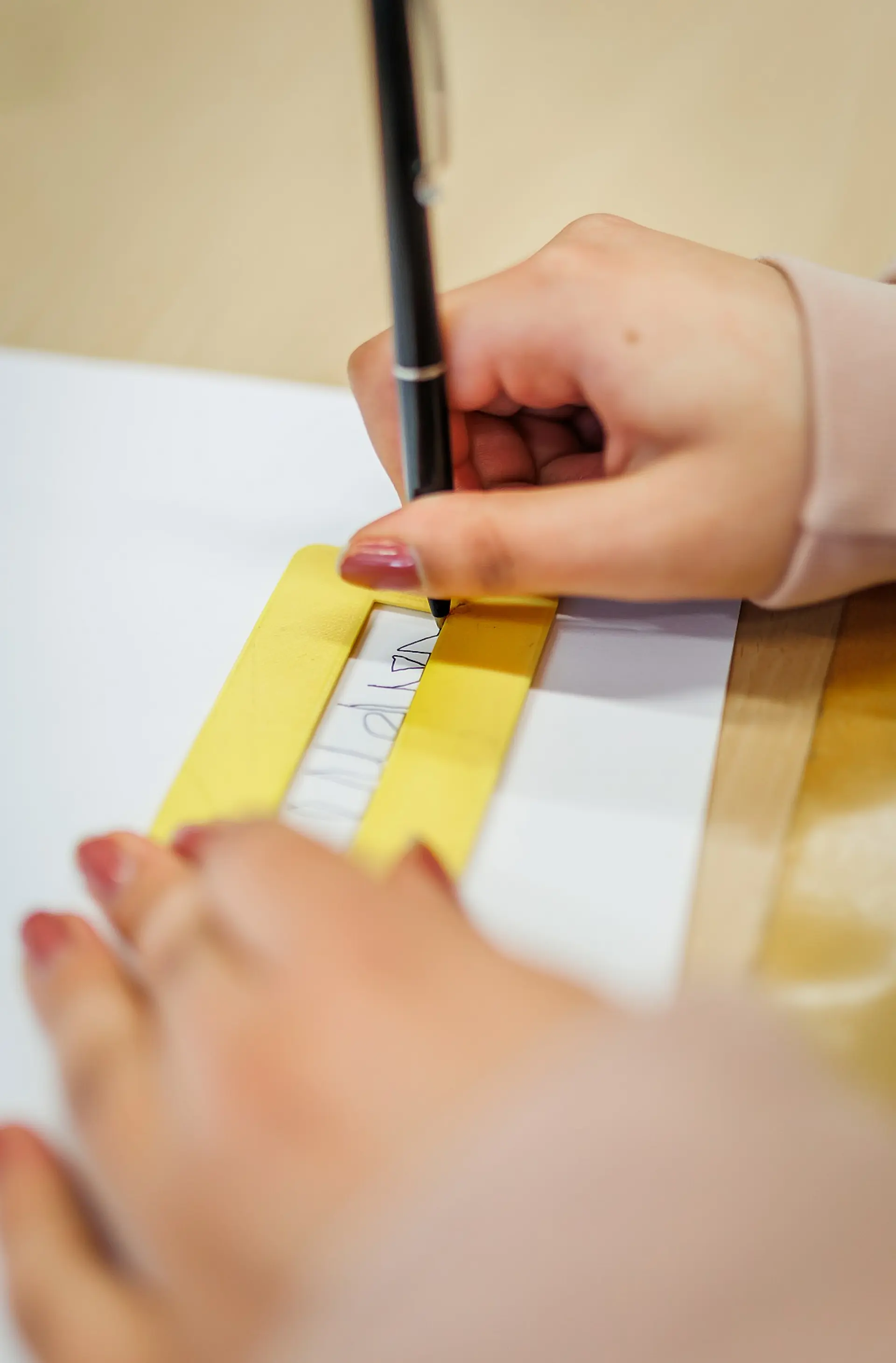 Die Hände einer Person. Mit der einen Hand hält sie eine Schablone zum Üben der eigenen Unterschrift, mit der anderen Hand schreibt sie mit einem Kugelschreiber.