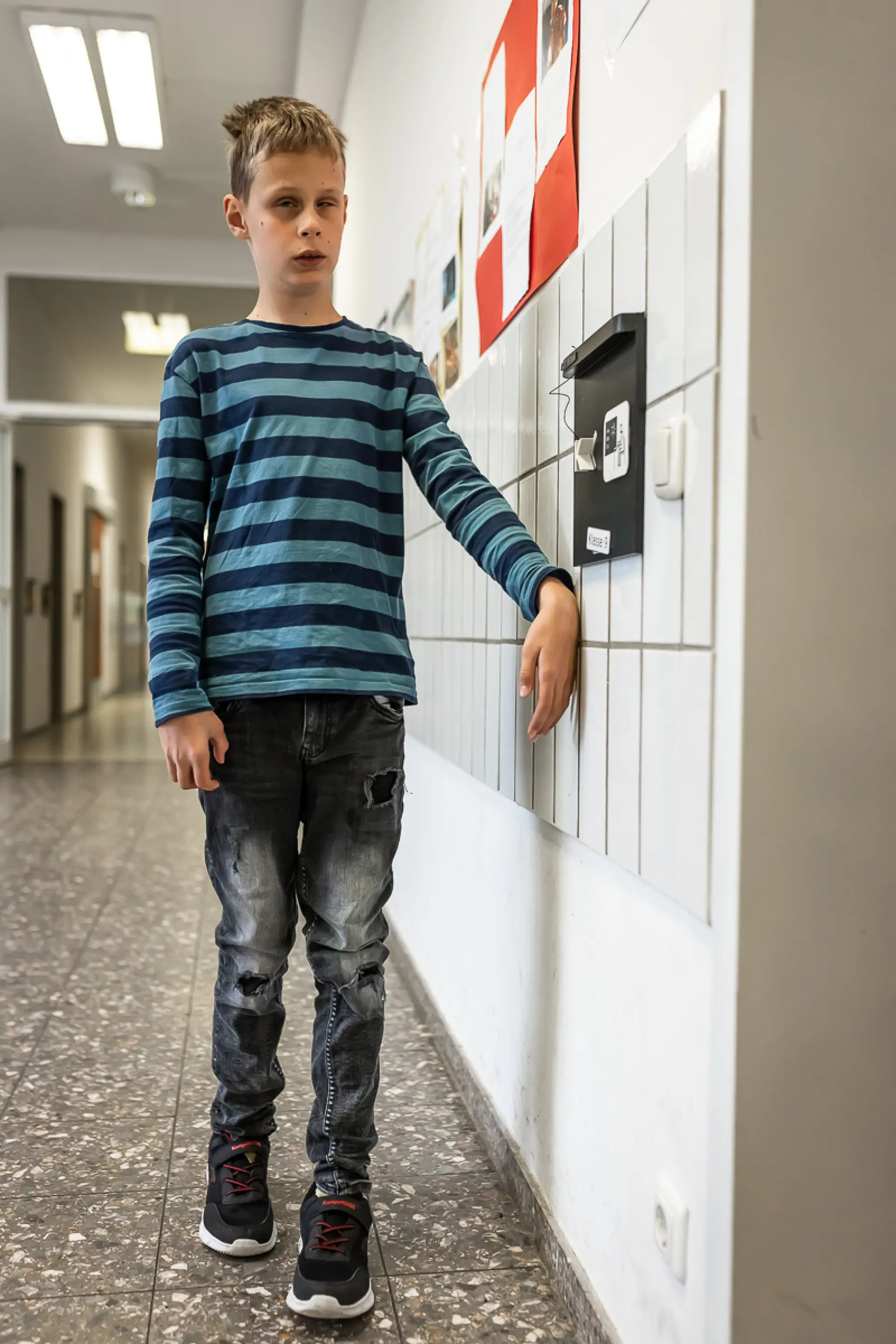 Ein Schüler mit Blindheit oder Sehbeeinträchtigung läuft im Gang des Schulgebäudes und ertastet mit dem Handrücken die Wand, damit er sich orientieren kann. 