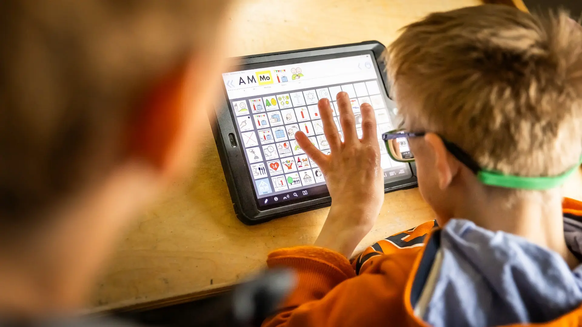 Ein Schüler klickt auf den Metacom-Symbolen auf seinem Tablet, die er zur Kommunikation mit der Lehrkraft neben ihm nutzt.