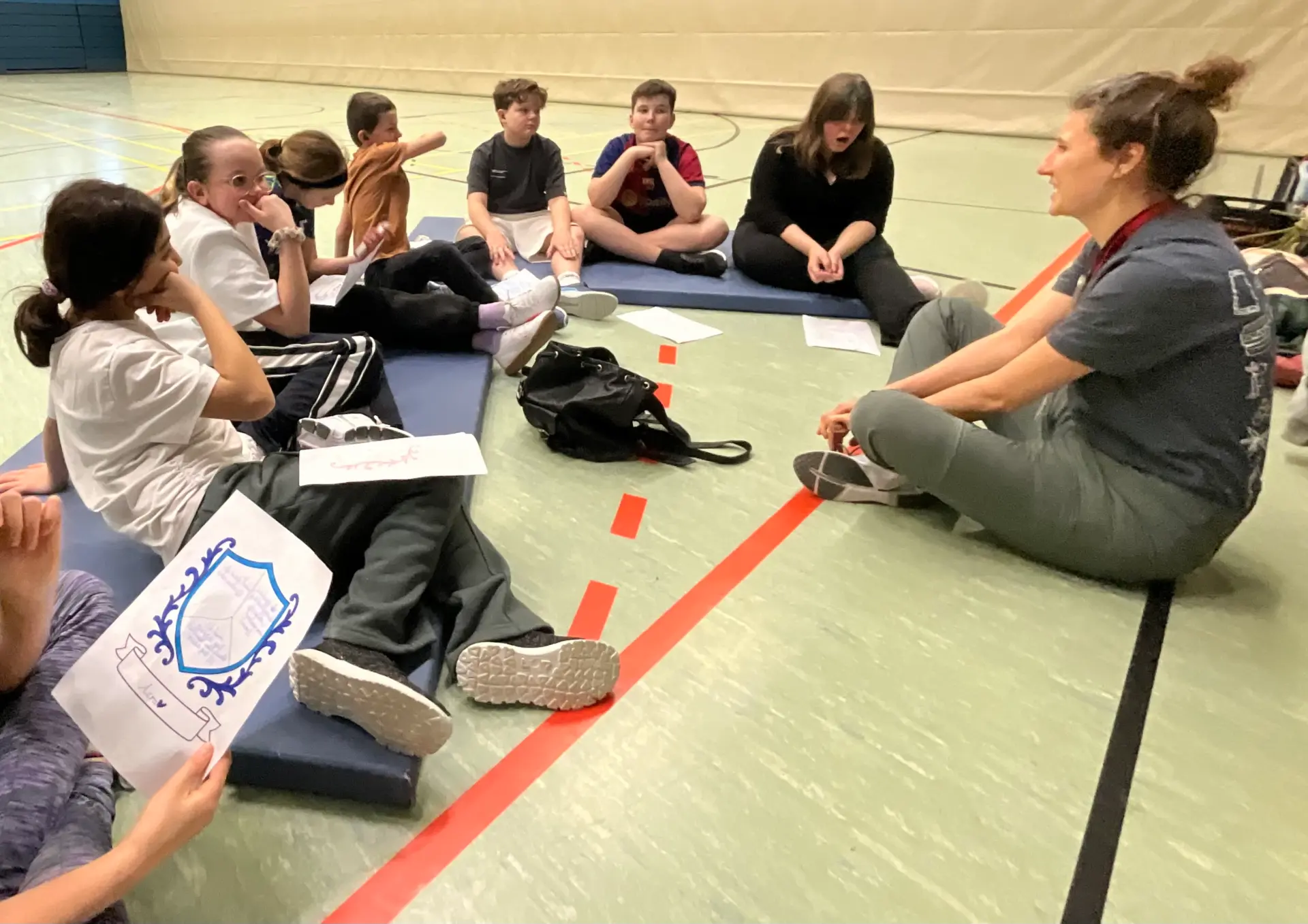 Projektwoche: Kinder sitzen im Kreis in der Turnhalle und reflektieren ihre Vorgehendweise bei einer Übung