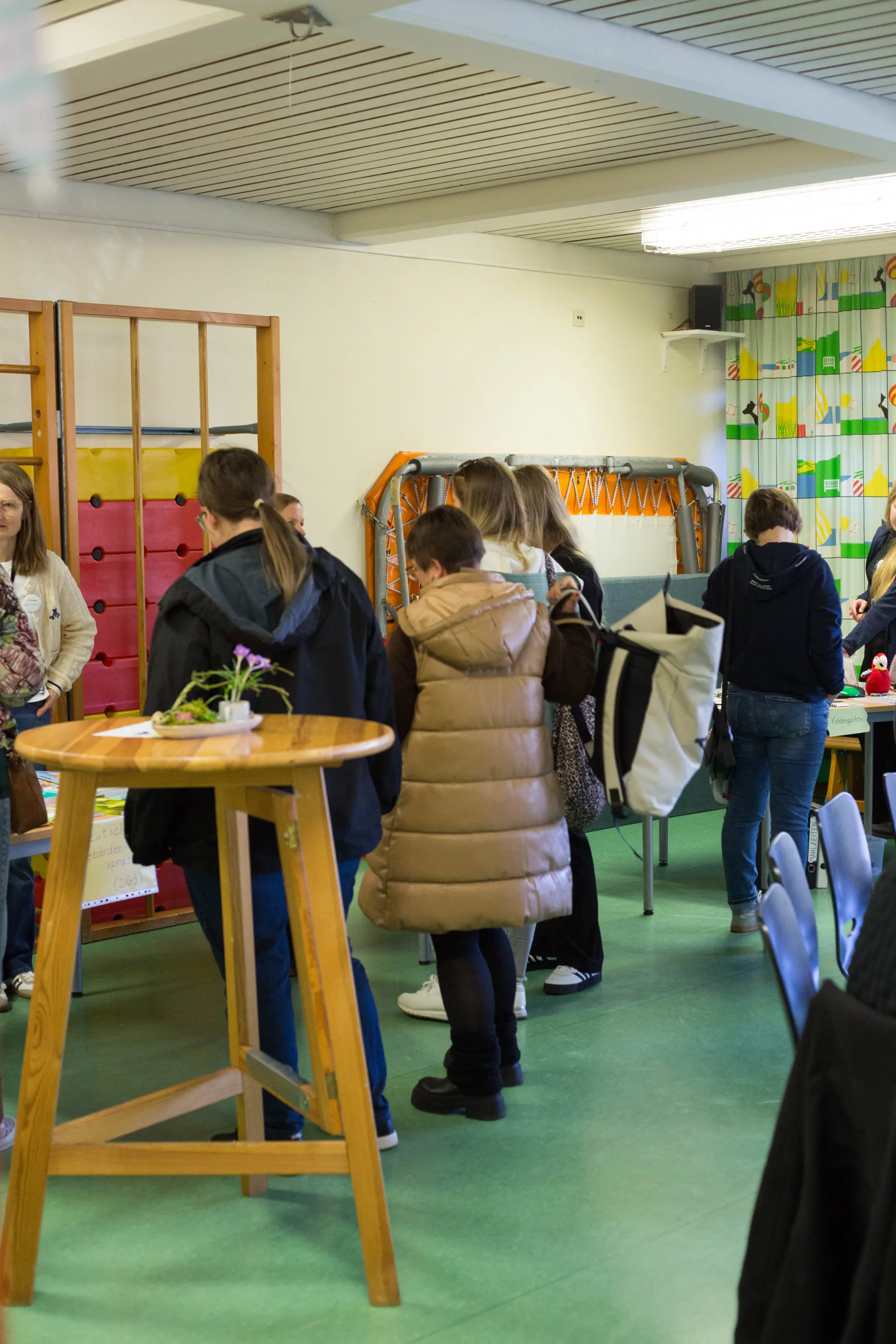 im Bewegungsraum schauen sich Erzieher*innen (von hinten zu sehen) Infomaterial auf Tischen an und sprechen mit den Lehrer*innen