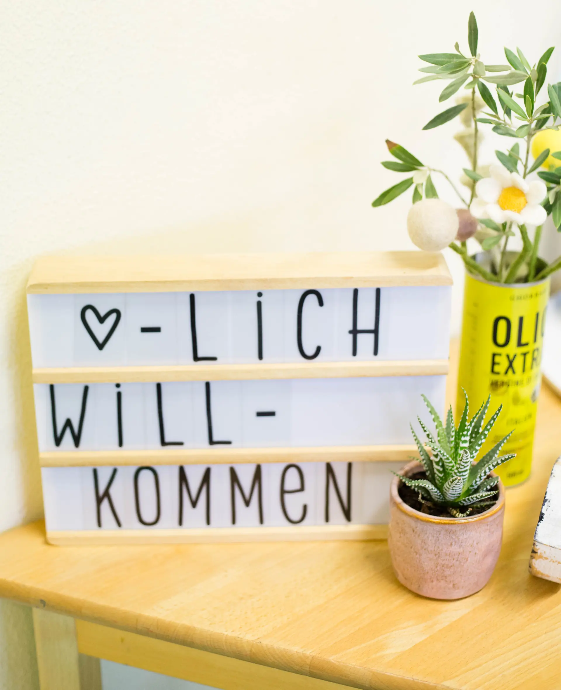 Auf einem Tisch stehen Blumen und eine Tafel mit der Aufschrift Herzlich Willkommen