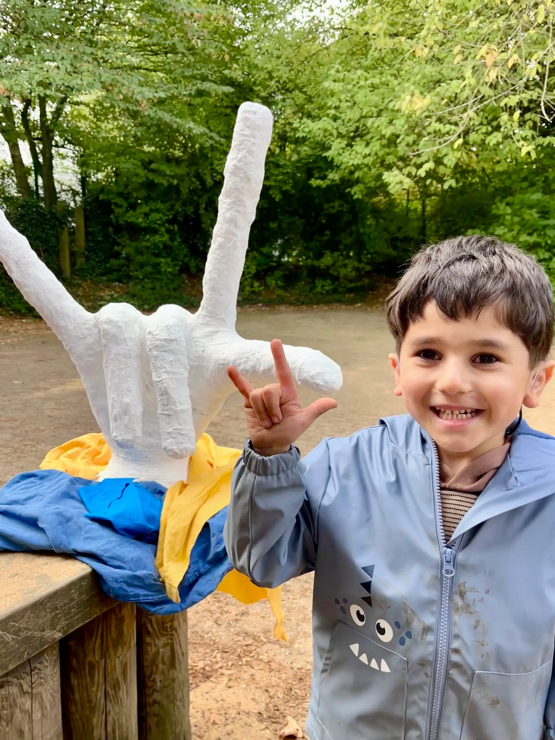 Kleiner Junge sitzt im Freien und gebärdet lächelnd "I love you"