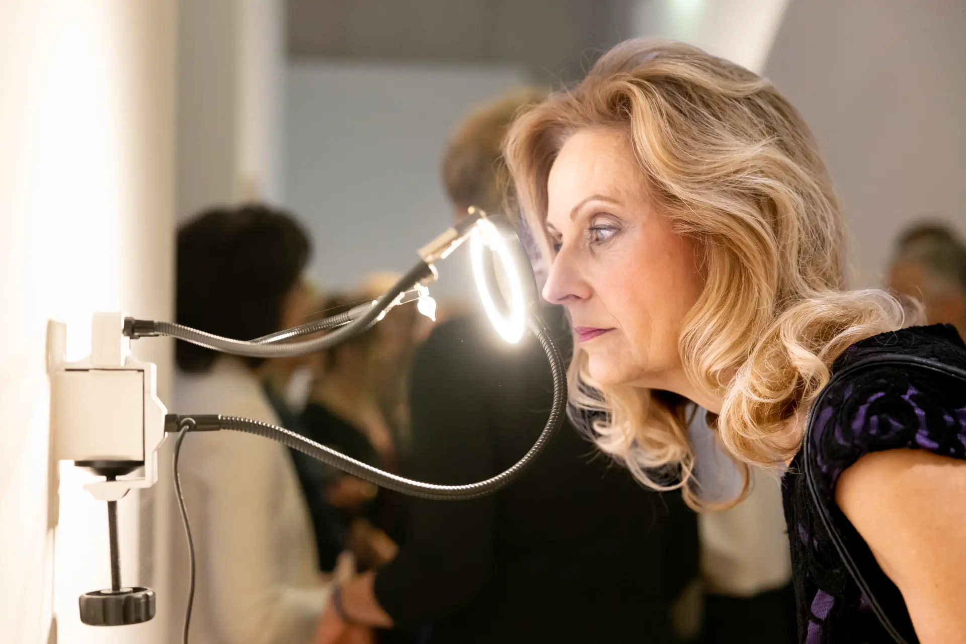 Besucherin betrachtet ein Kunstwerk durch eine beleuchtete Lupe.