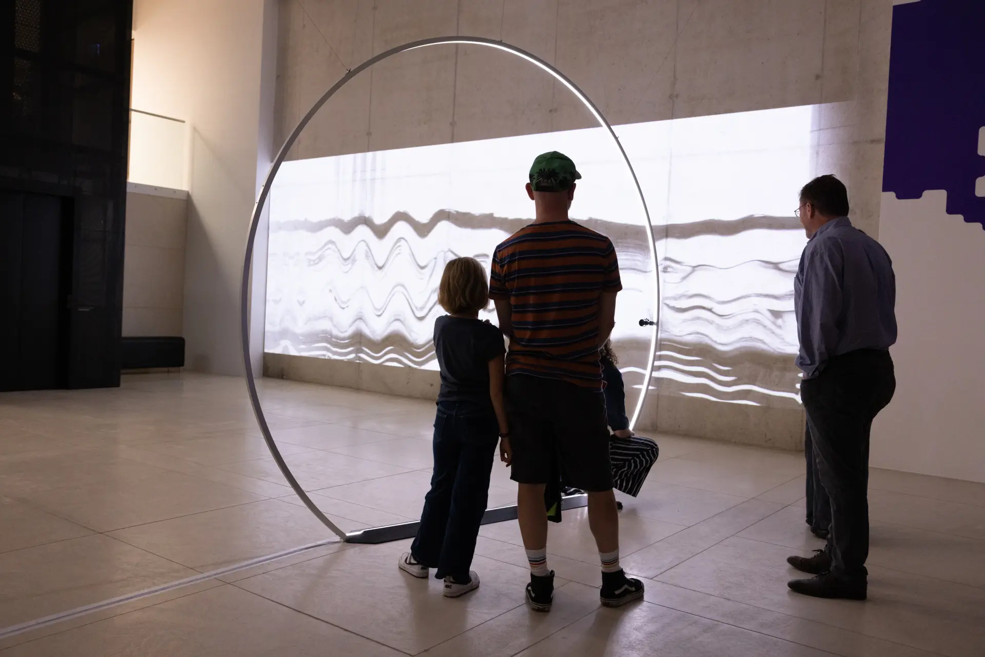 Zwei Männer und ein Kind blicken auf eine Projektion.