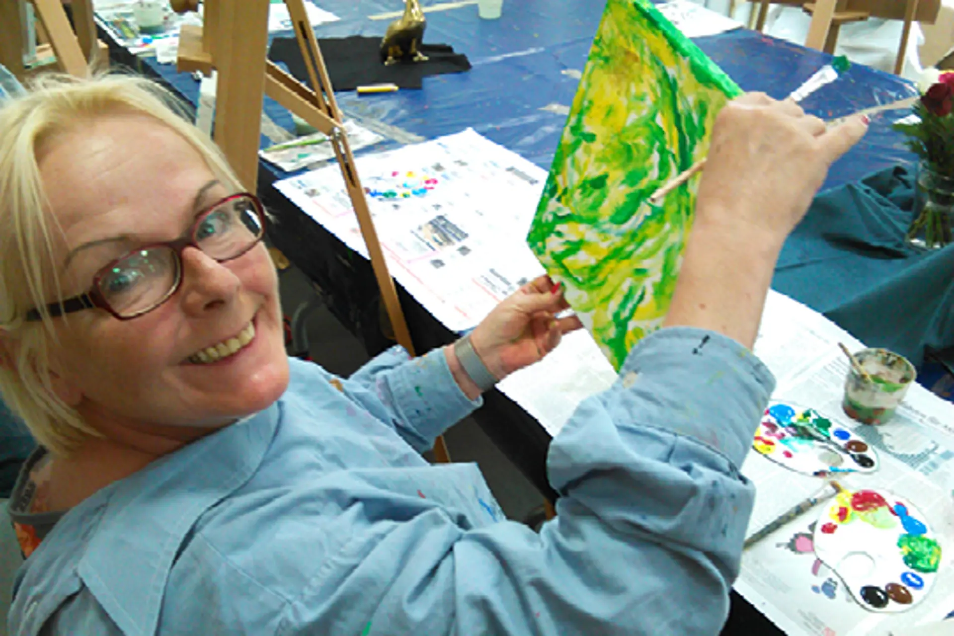 Eine Frau präsentiert in der Museumswerkstatt lächelnd ihr Gemälde