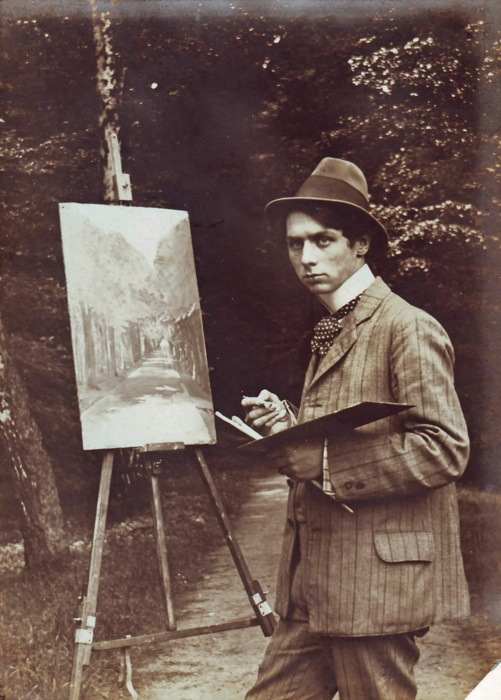 Ein junger Max Ernst steht mit vor einer Staffelei in einem Park.