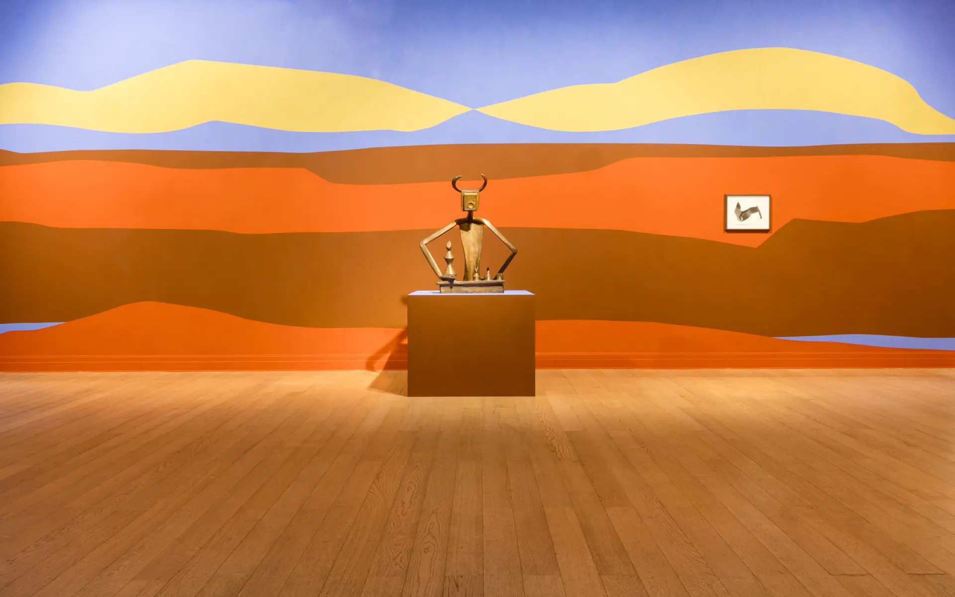 Skulptur von Max Ernst vor einer bemalten Wand, die an eine Wüste erinnert