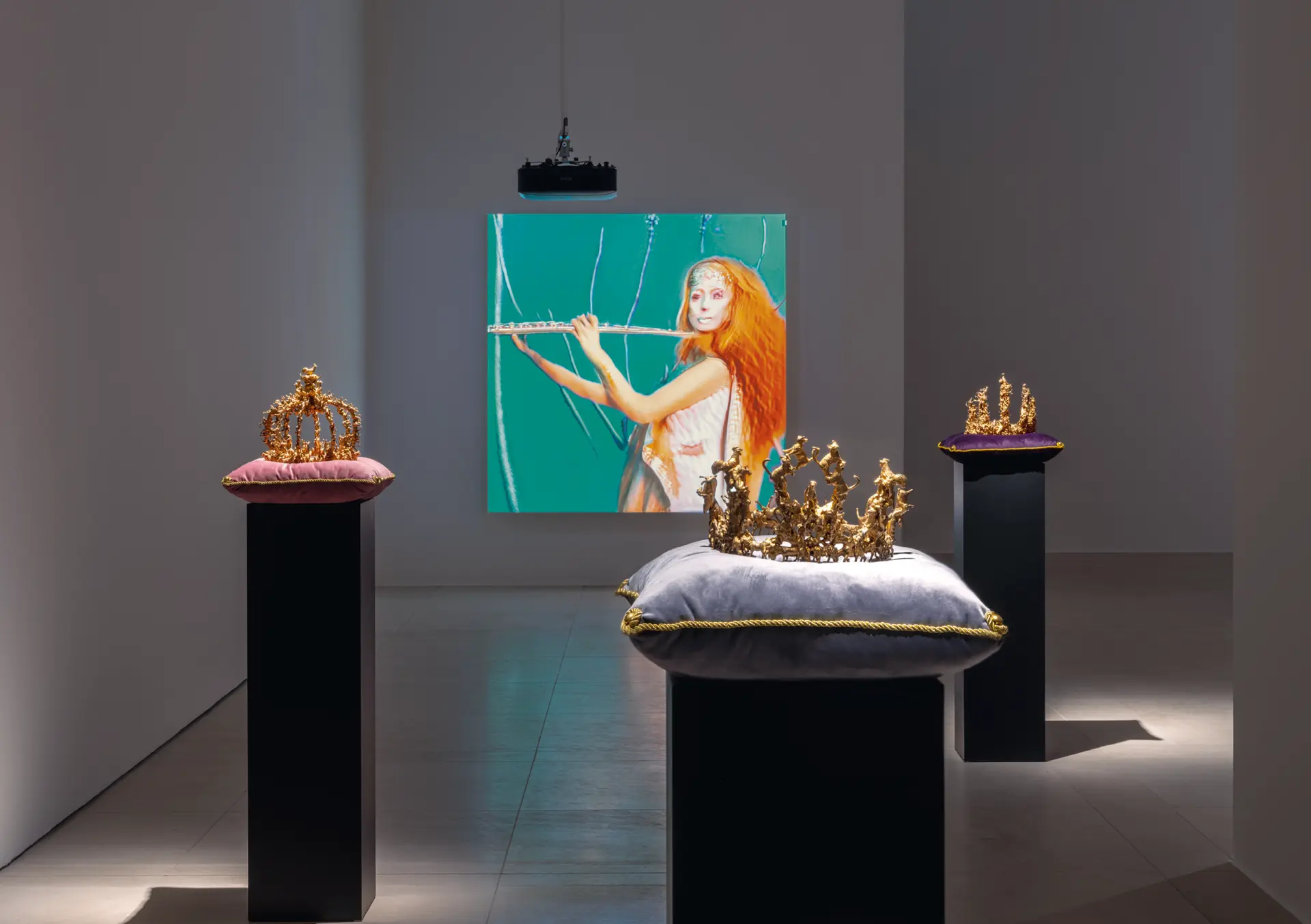 Ausstellungsansicht mit mehreren goldenen Kronenskulpturen auf Kissen liegend